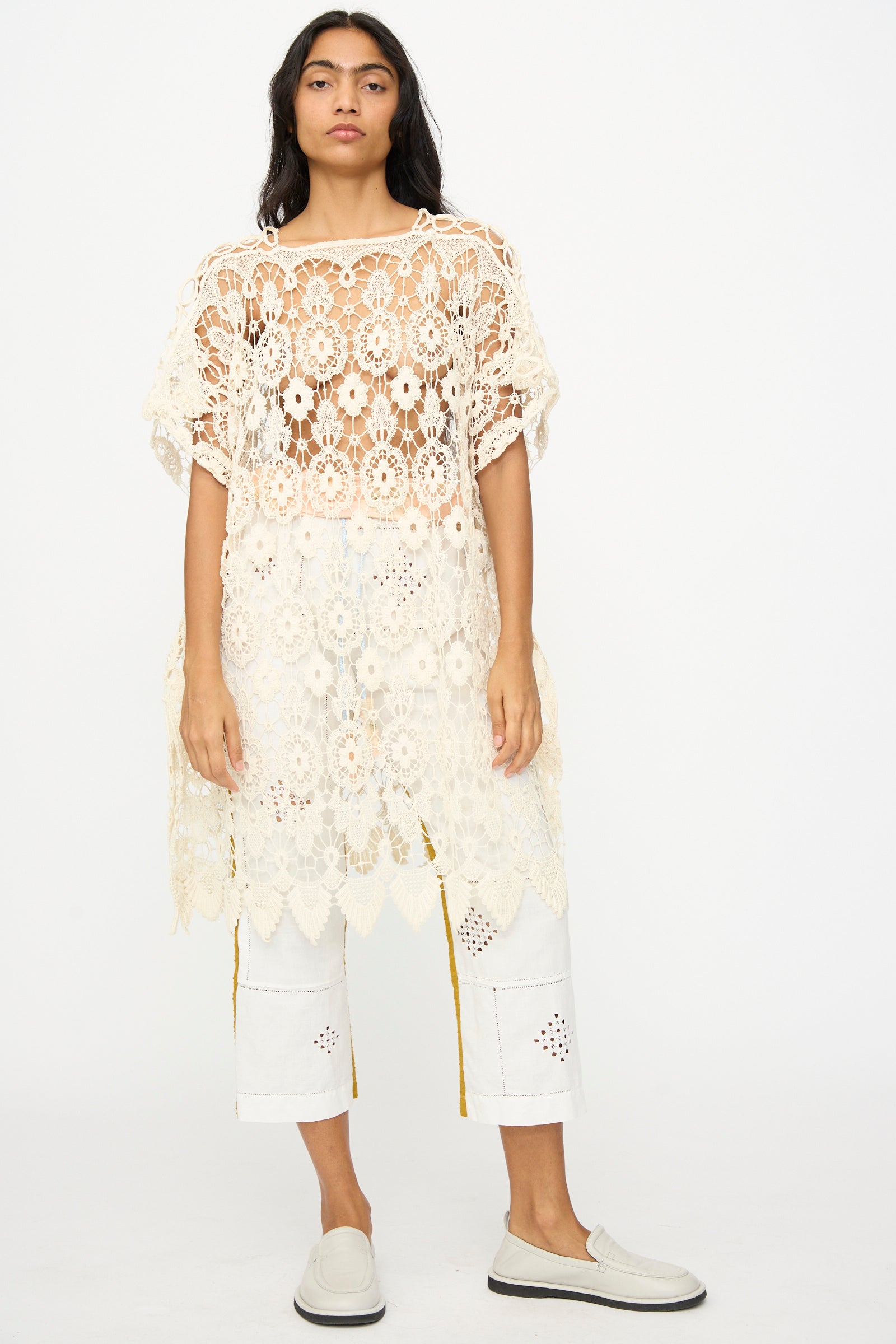 A person stands facing forward in a Thank You Have A Good Day Antique Lace Midi Caftan, layered over white cropped pants and white slip-on shoes, set against a plain background.