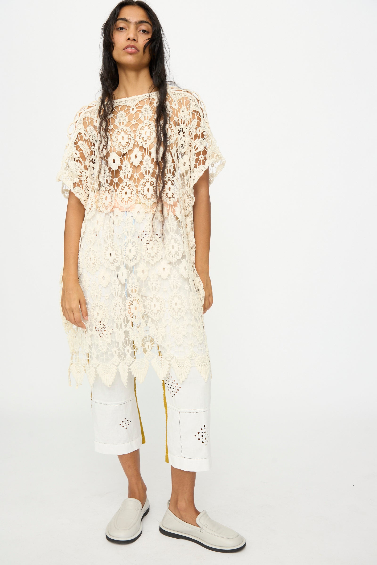 A person stands against a plain background wearing the Antique Lace Midi Caftan by Thank You Have A Good Day in cream crochet, styled over white cut-out detail pants and slip-on shoes.
