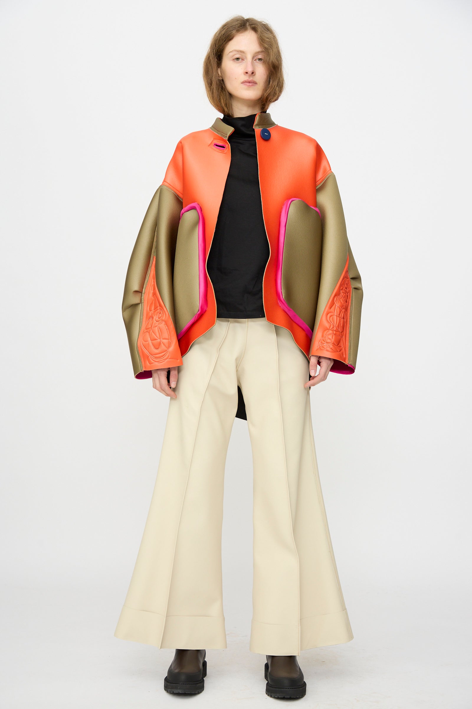 A person poses against a plain backdrop in the Thank You Have A Good Day Color block Cropped Parka, flared beige pants, a black top, and black boots.