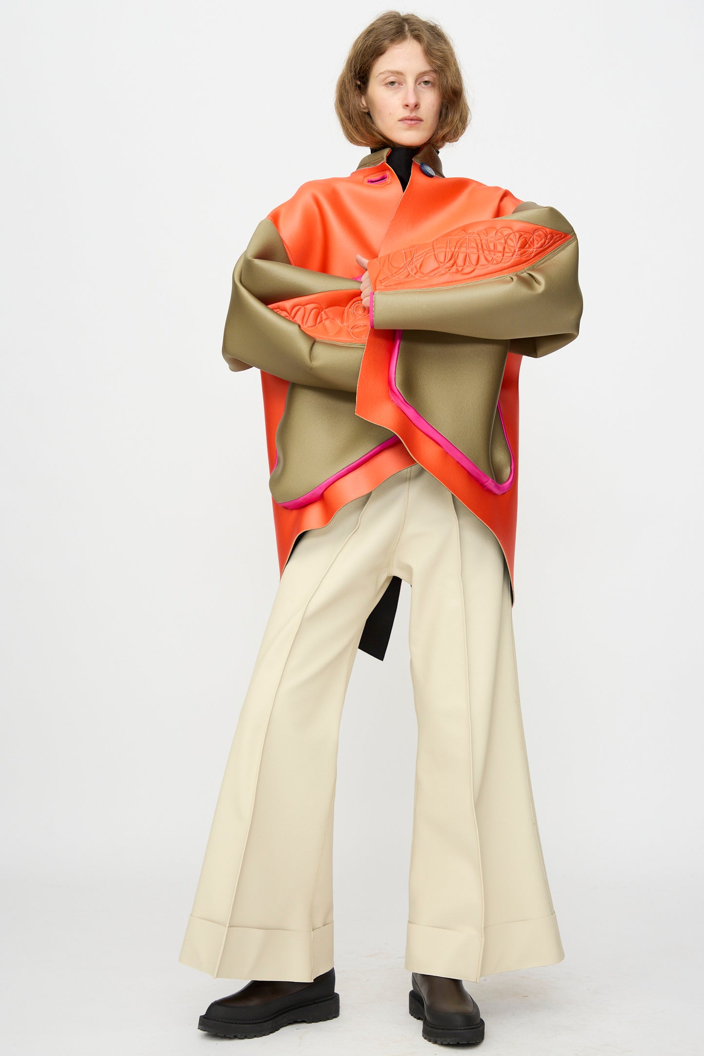 A person stands against a white background wearing the Thank You Have A Good Day Color block Cropped Parka in orange, olive, and pink, paired with wide-leg cream pants and black shoes.