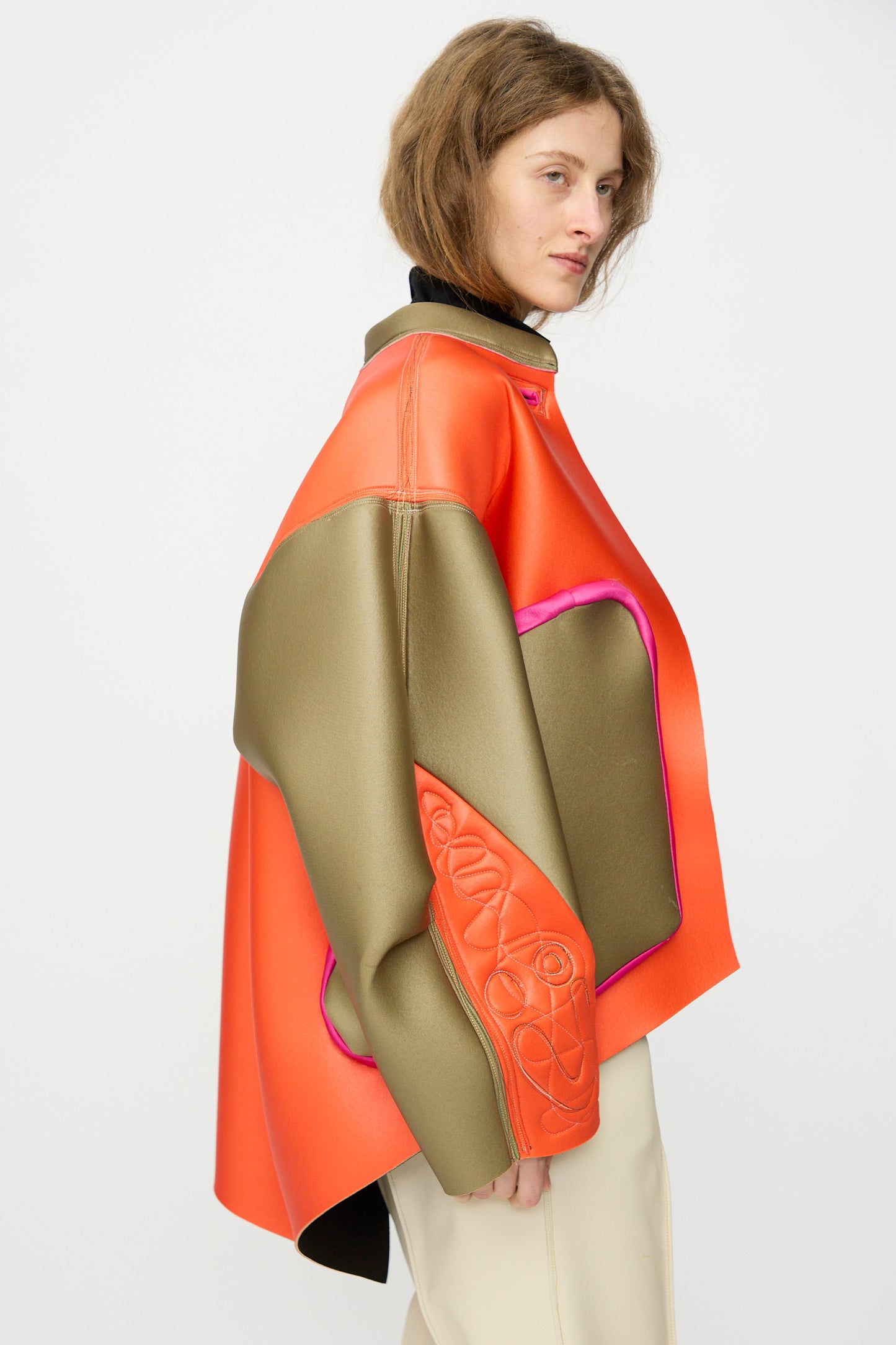 A person wears the Thank You Have A Good Day Color block Cropped Parka in orange and olive green with pink trim and quilted sleeves, standing against a plain white background.