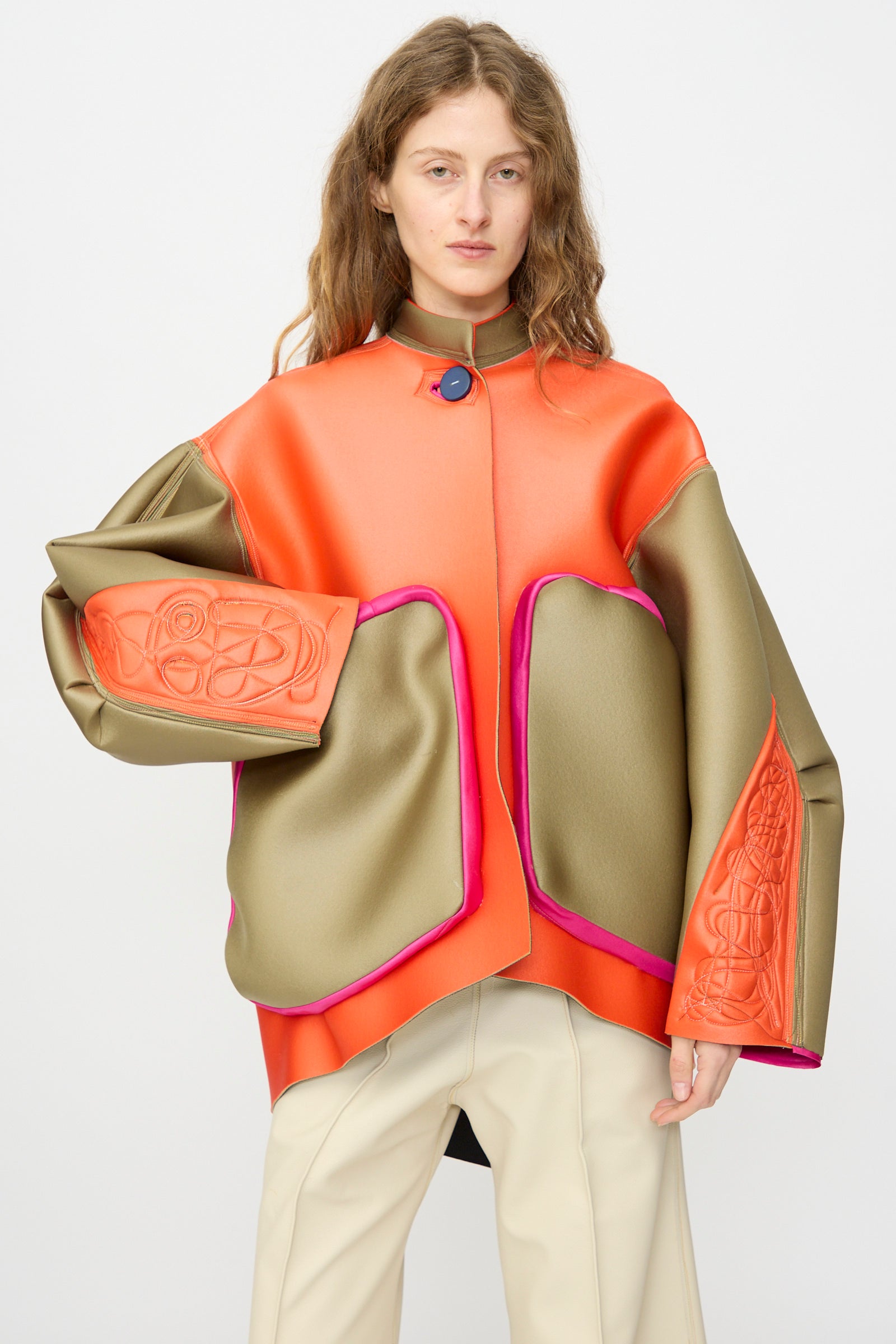 Model wears the Thank You Have A Good Day Color block Cropped Parka in orange, olive green, and pink with oversized sleeves and abstract patterns, paired with beige pants, against a plain background.