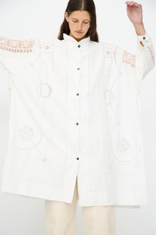 A person wearing the Heart and Flower Oversized Oxford by Thank You Have A Good Day—an oversized oxford cotton shirt dress with embroidered geometric and floral patterns and subtle lace details—stands with arms slightly raised.