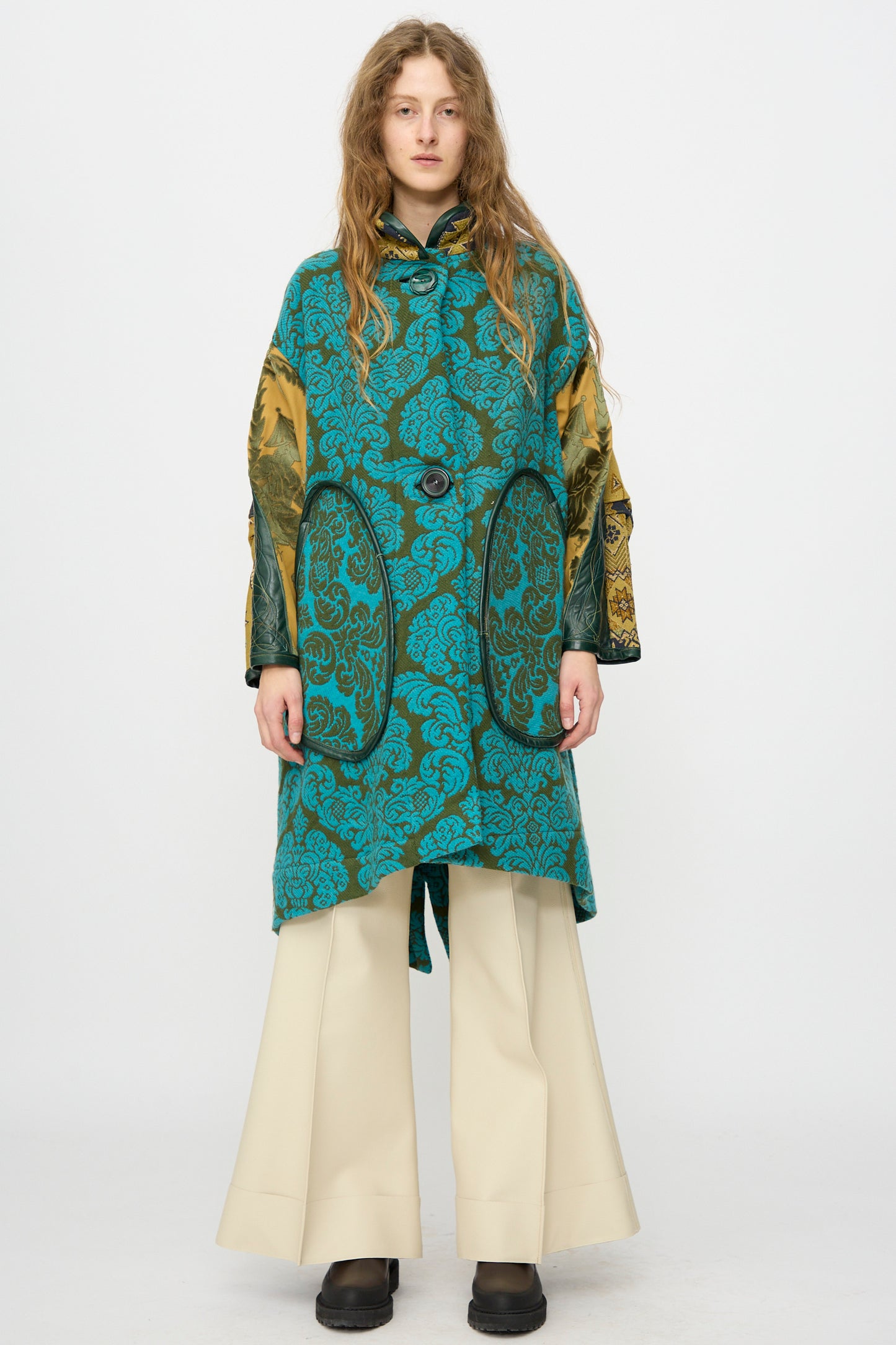 A person stands facing forward against a plain white background, wearing the Thank You Have A Good Day Patchwork Fishtail Parka with gold sleeves and vintage buttons, paired with wide-leg cream pants and black shoes.