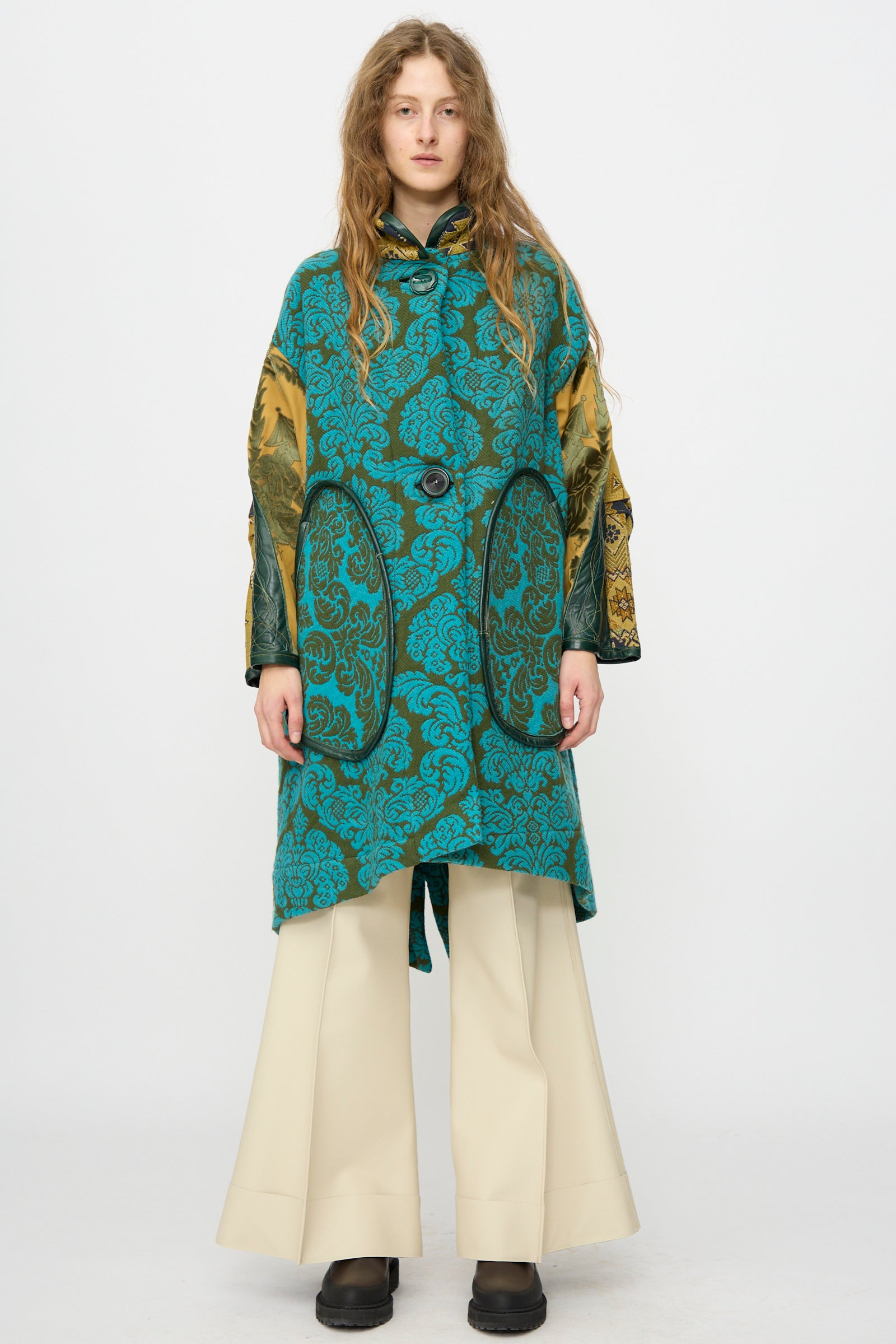 A person stands facing forward against a plain white background, wearing the Thank You Have A Good Day Patchwork Fishtail Parka with gold sleeves and vintage buttons, paired with wide-leg cream pants and black shoes.