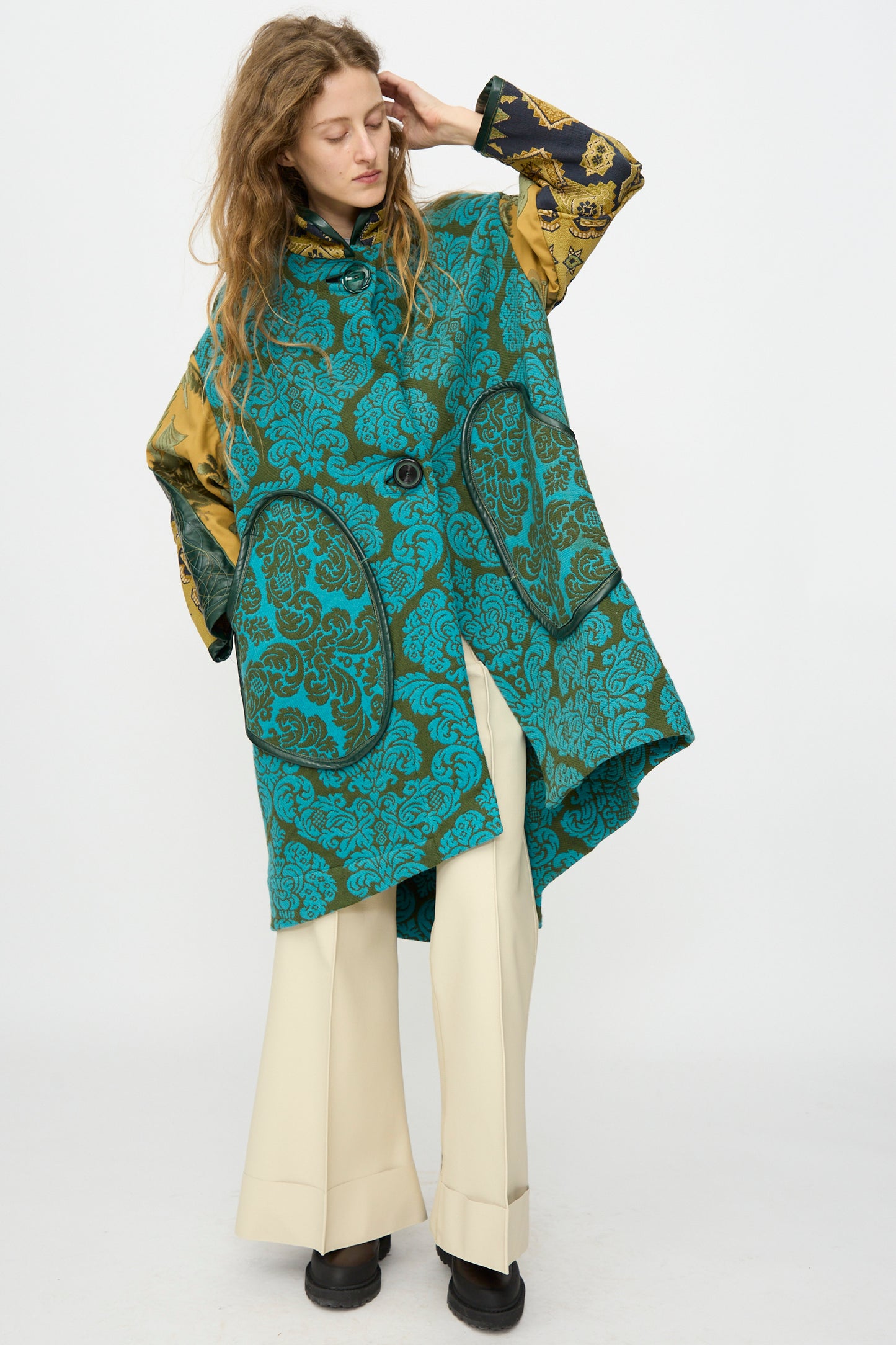 A person models the Thank You Have A Good Day Patchwork Fishtail Parka with gold and black sleeves, vintage buttons, cream wide-leg pants, and black shoes, posing against a plain white background.