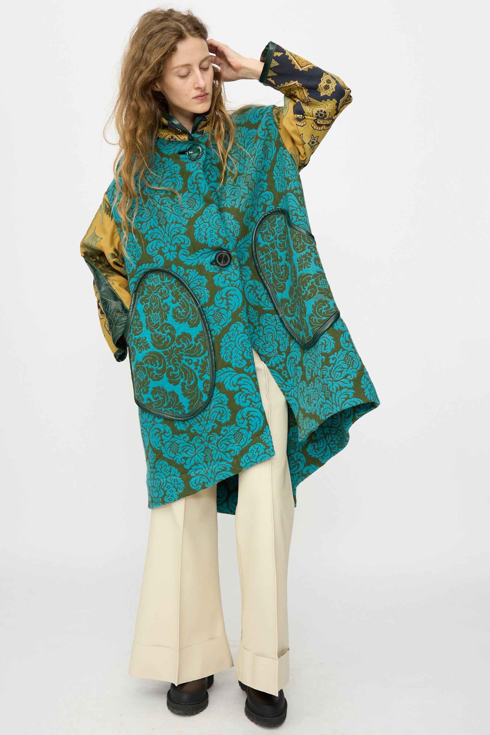 A person models the Thank You Have A Good Day Patchwork Fishtail Parka with gold and black sleeves, vintage buttons, cream wide-leg pants, and black shoes, posing against a plain white background.