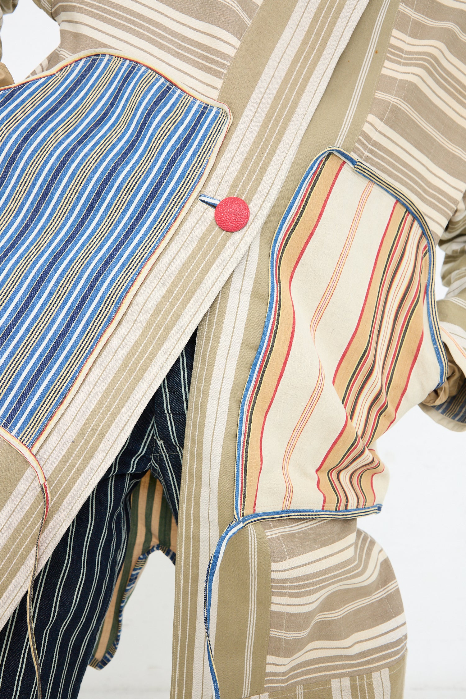 A close-up of a textile artwork featuring an assemblage of vintage cottons and antique Thank You Have A Good Day French Ticking Fishtail Parka, with conspicuous stitching details and a red circular accent.