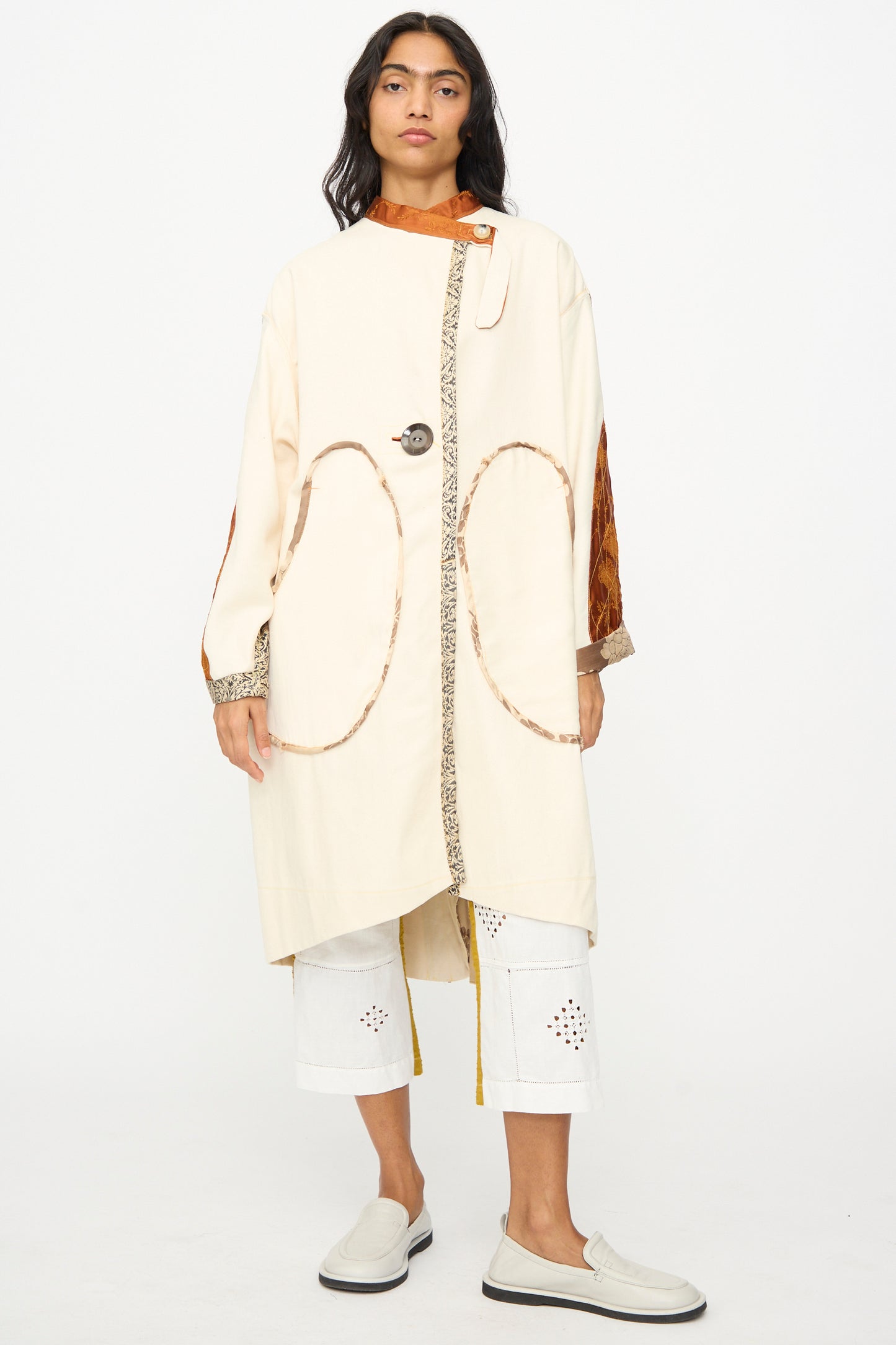 Wearing the Patchwork Parka by Thank You Have A Good Day—cream with circular patterns, vintage buttons, and printed trim—over white cropped pants with cutouts and slip-on shoes for a handmade Tribeca vibe.
