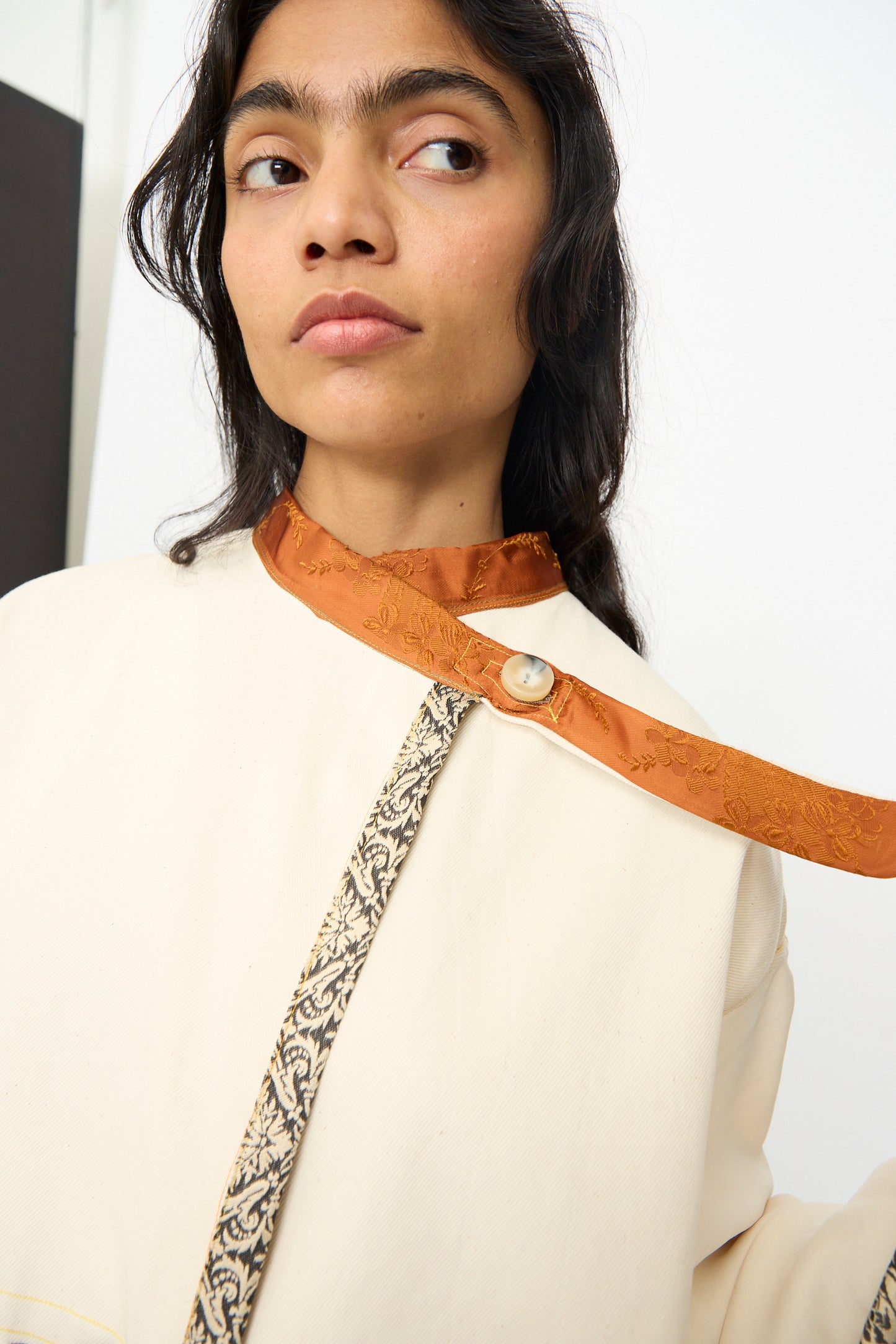 A woman wears the Patchwork Parka by Thank You Have A Good Day—a handmade cream-colored top with an orange collar, vintage button, and black-and-white trim.