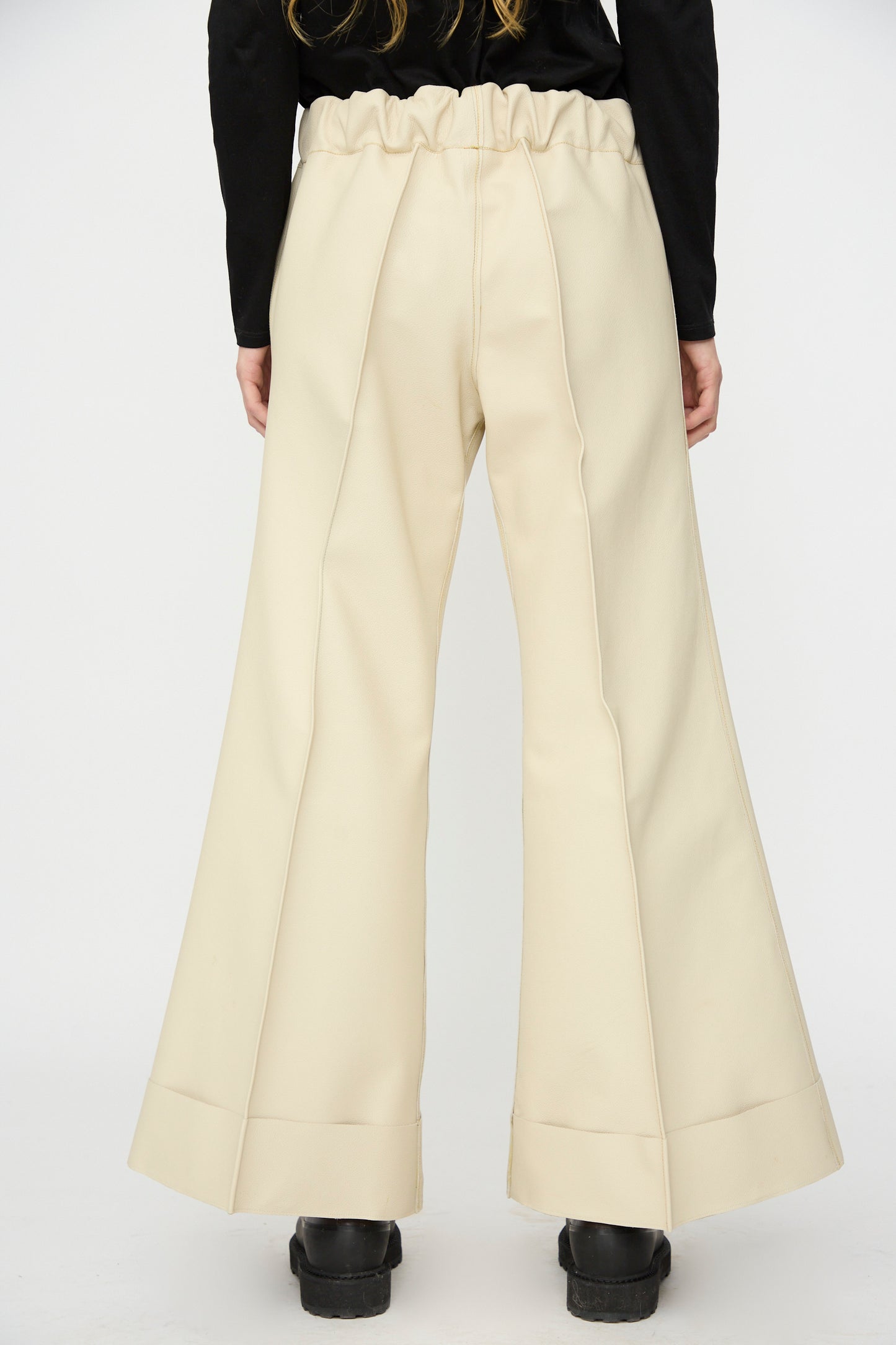 Model wearing Thank You Have A Good Day's Pierrot Flare Trouser in Leather—high-waisted, relaxed fit, wide-leg beige pants with a ruffled waistband—paired with black shoes and shown from the back against a plain background.