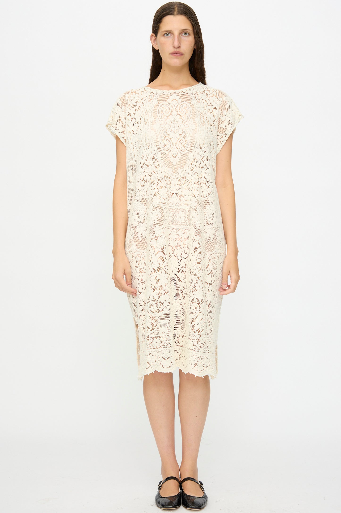 A person stands facing forward in the Thank You Have A Good Day Quaker Lace Caftan Midi Pullover, a cream-colored, knee-length, short-sleeved dress, with black flats against a plain white background.