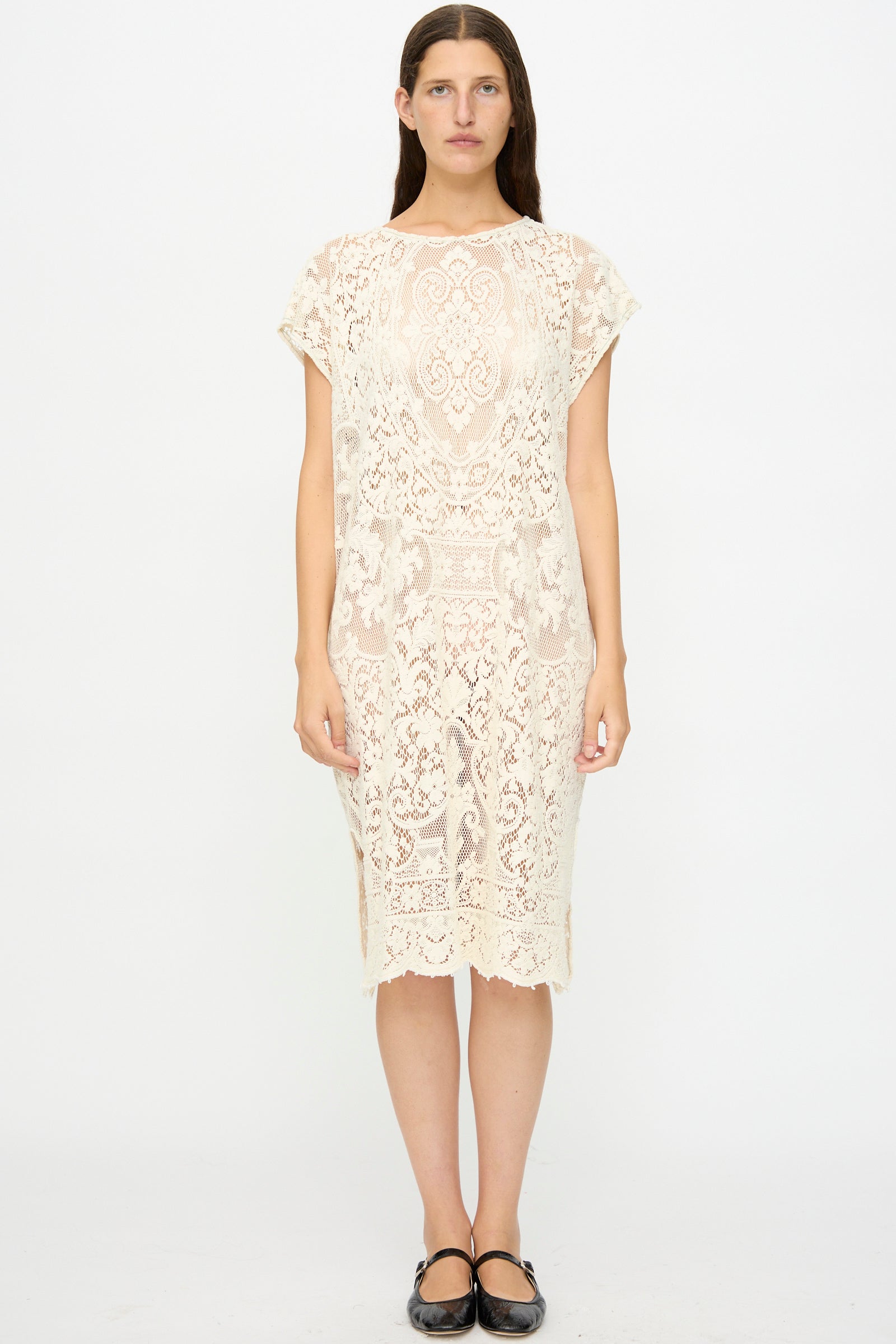 A person stands facing forward in the Thank You Have A Good Day Quaker Lace Caftan Midi Pullover, a cream-colored, knee-length, short-sleeved dress, with black flats against a plain white background.