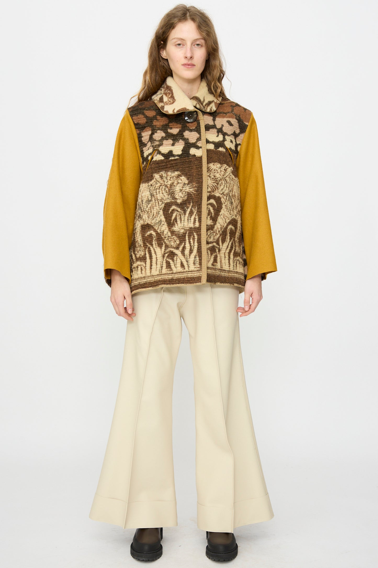 A woman stands facing forward against a plain white background, wearing the Tiger Topper Jacket by Thank You Have A Good Day, featuring vintage 1930s-inspired animal motifs, paired with cream wide-leg pants and black shoes.