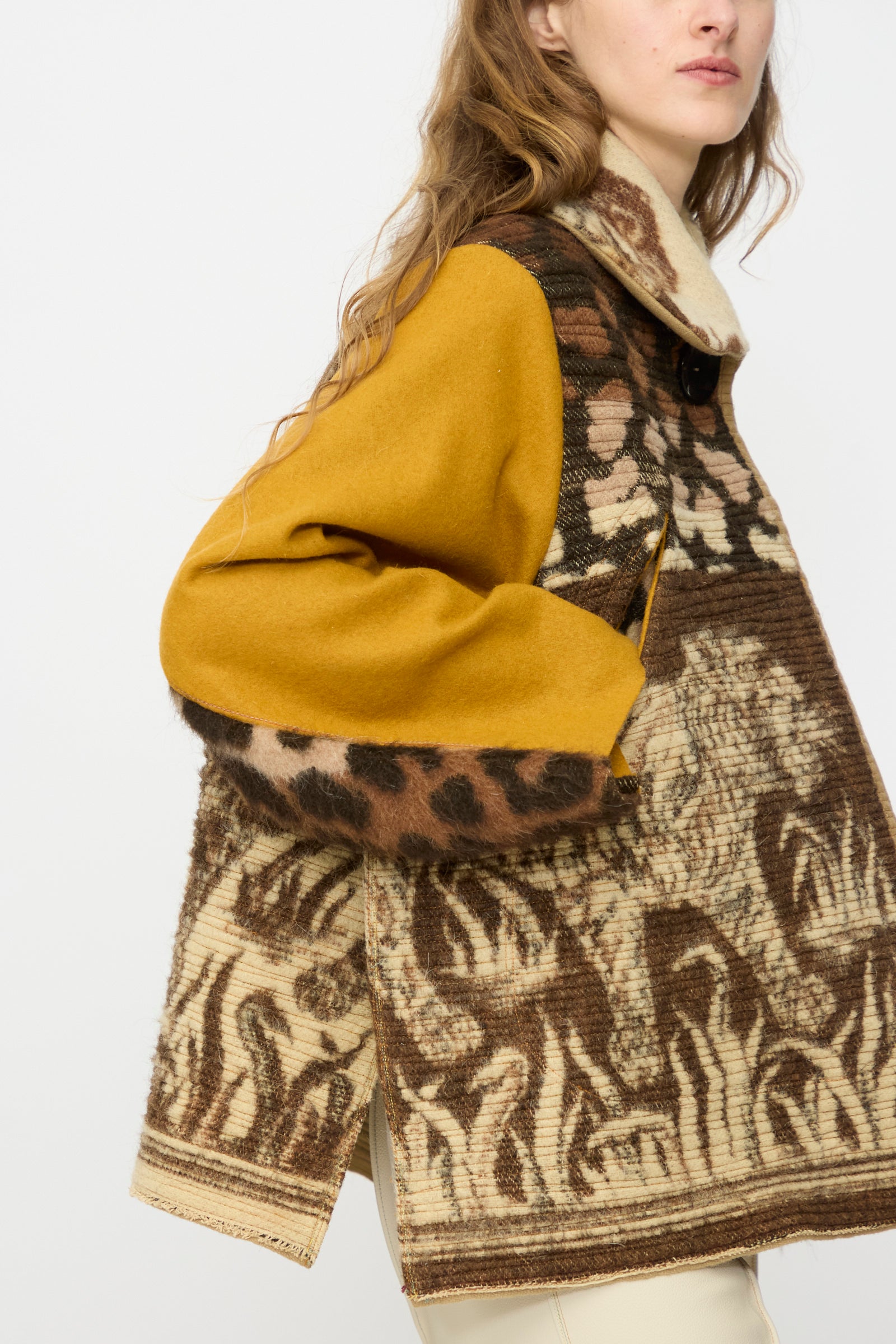 A person wearing the Tiger Topper Jacket by Thank You Have A Good Day—featuring a vintage-inspired brown and beige pattern with mustard yellow sleeves—stands against a plain white background.