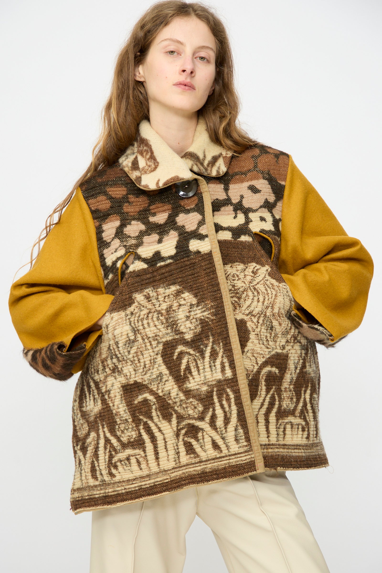A person wears the Tiger Topper Jacket by Thank You Have A Good Day, featuring handmade lion and floral designs with mustard sleeves, paired with cream pants against a plain light background.