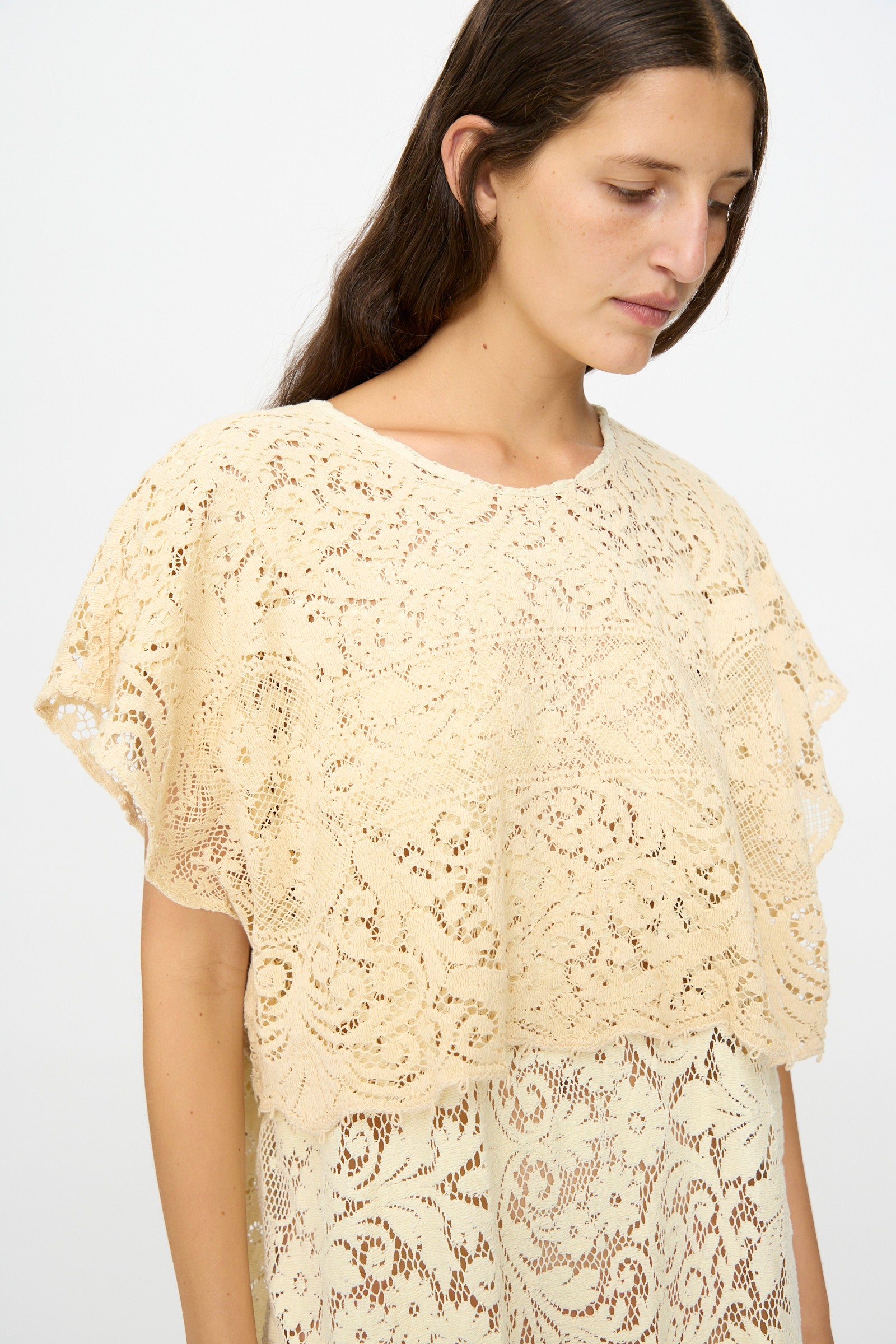 A person with long brown hair models the Thank You Have A Good Day Tilda Gown in Quaker Lace, a cream-colored maxi dress with short sleeves, standing against a plain white background.