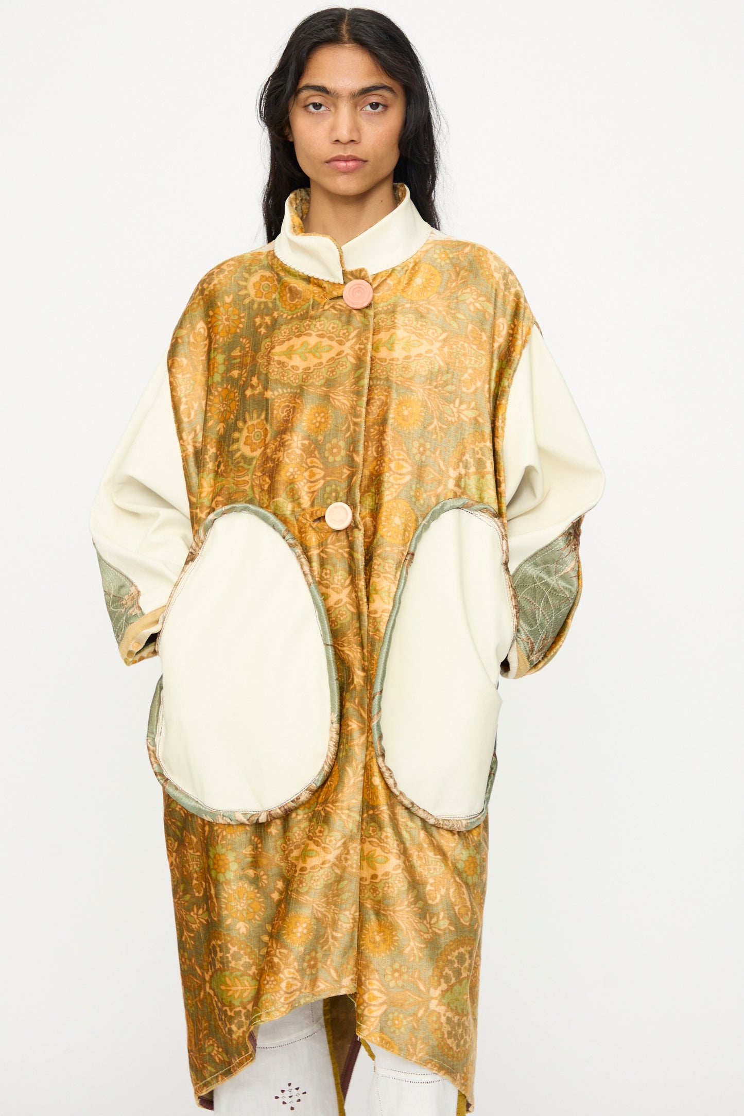 A person wears the Velvet and Leather Fishtail Parka by Thank You Have A Good Day, featuring vintage velvet, large oval pockets, and a gold patterned front, standing against a plain white background.