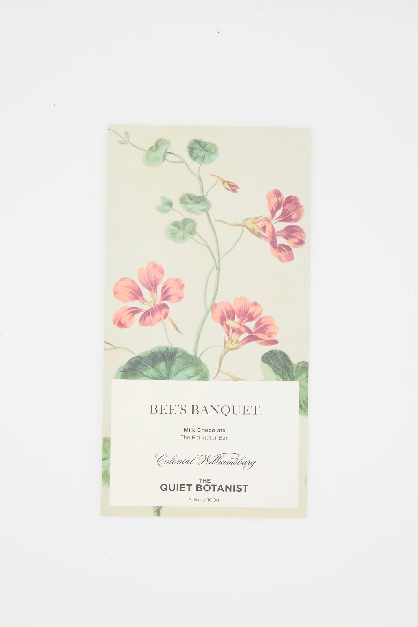 The beige packaging of The Quiet Botanist's Bee's Banquet Bar features a botanical design with pink flowers and green leaves, labeled as "Milk Chocolate" with Bee Pollen, against a white background. 