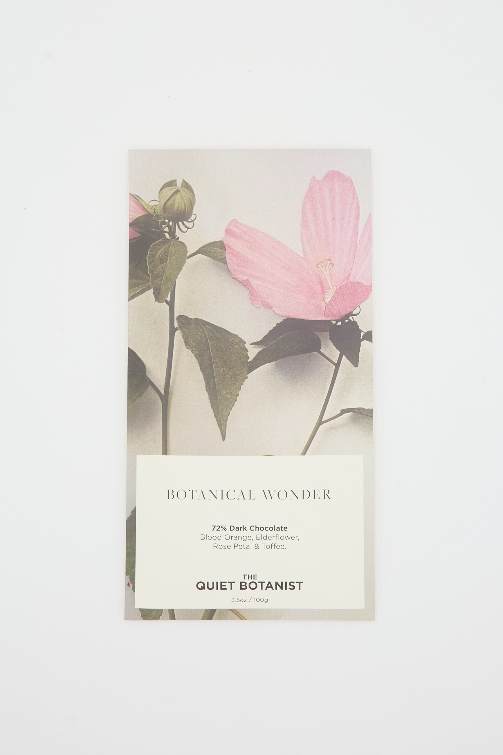 A botanical-themed chocolate bar from The Quiet Botanist, encased in a paper wrapper adorned with pink flowers and green leaves. The label reads "Botanical Wonder Bar" and describes the flavor: 72% dark chocolate with various floral and fruit notes, including hints of blood orange and elderflower.