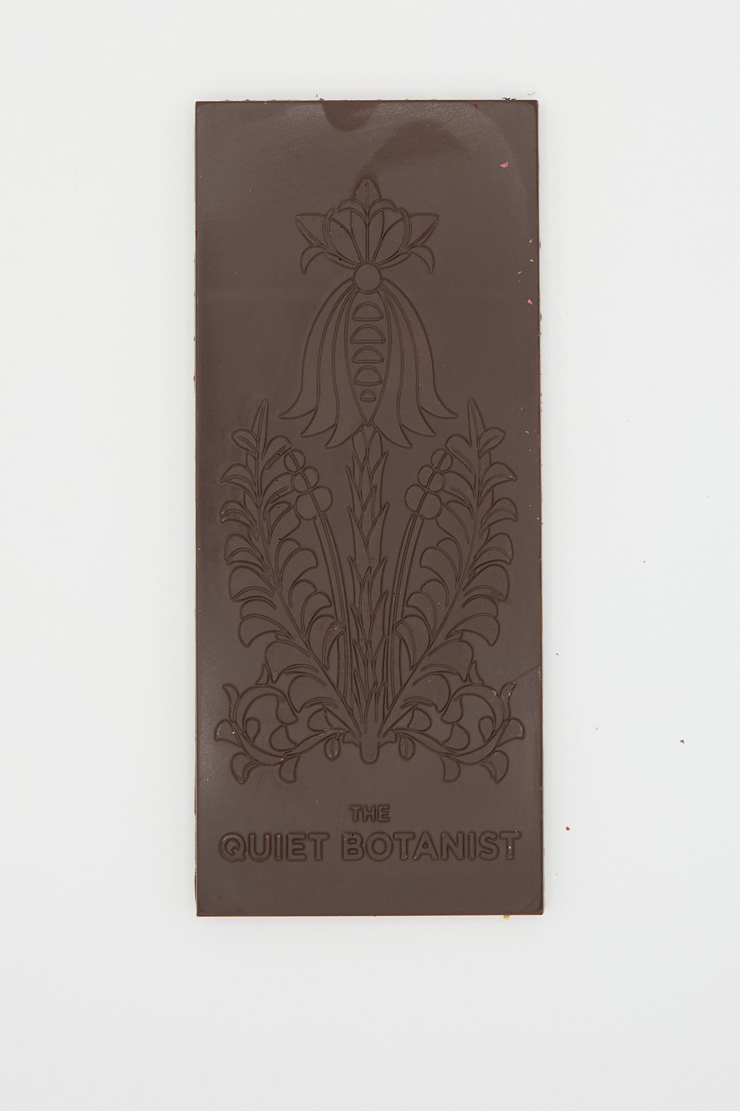 A Botanical Wonder Bar dark chocolate featuring intricate floral designs with "The Quiet Botanist" engraved at the bottom.