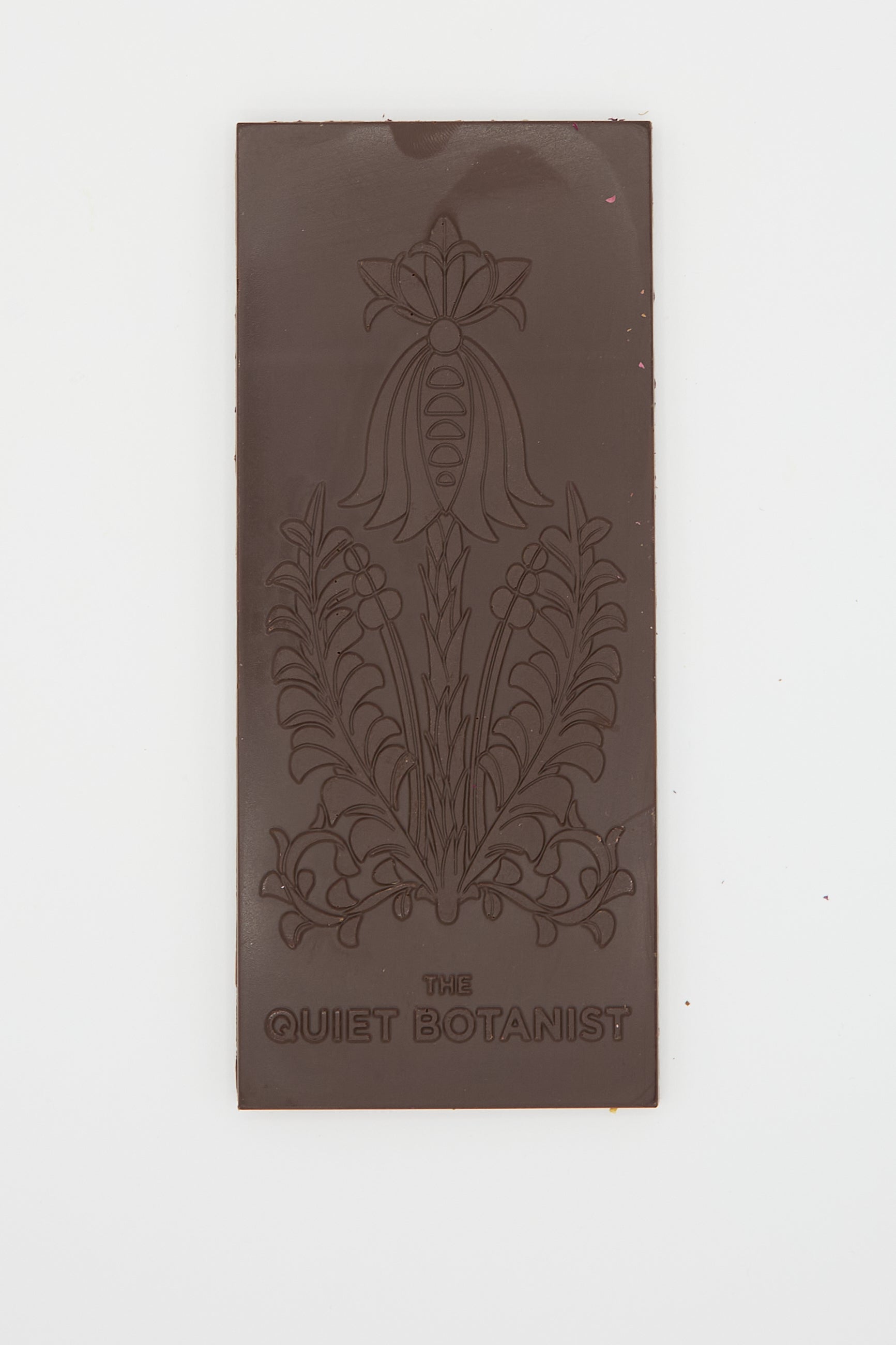 A Botanical Wonder Bar dark chocolate featuring intricate floral designs with "The Quiet Botanist" engraved at the bottom.