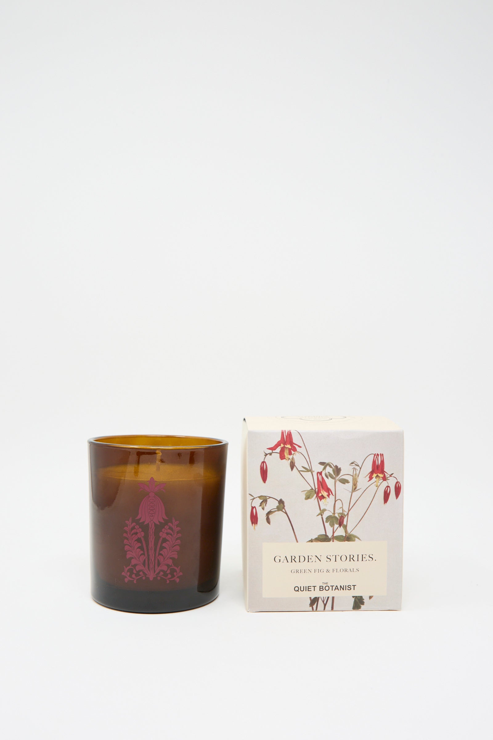 A brown glass candle with a floral design, crafted from phthalate-free coconut wax, sits beside a box labeled "Garden Stories Candle" by The Quiet Botanist, adorned with botanical illustrations.