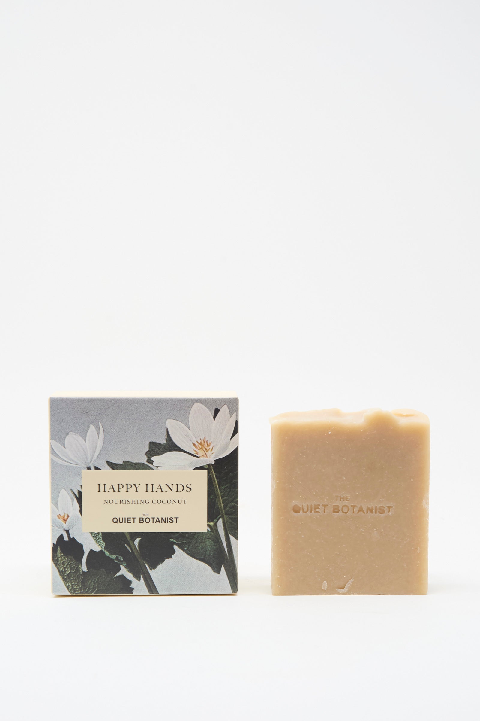 The Quiet Botanist Happy Hands Nourishing Coconut Soap Bar is shown with its box featuring botanical designs. This vegan, handmade soap from Turkey is perfect for nourishing your hands.