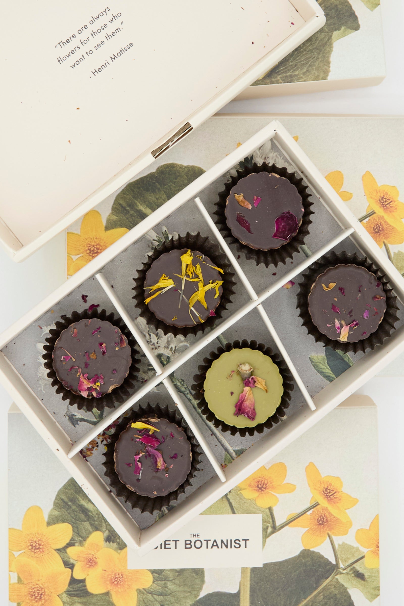 A box of six Holiday Bon Bons by The Quiet Botanist, each adorned with rose petals and featuring flavors such as dark chocolate and blood orange caramel, displayed on a floral-themed surface.