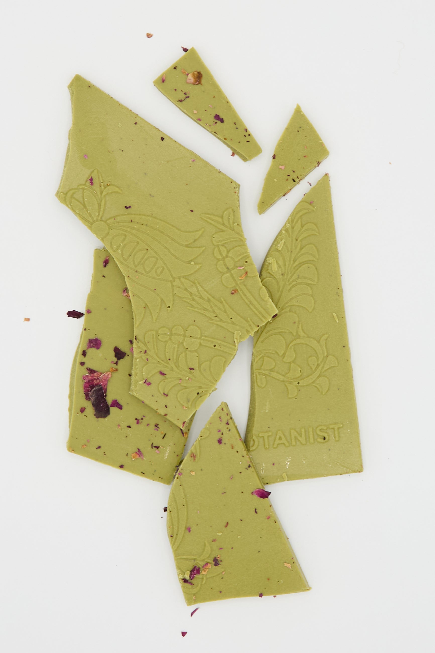 Fragments of The Quiet Botanist's Matcha Rose Chocolate Bar, adorned with floral patterns and rose petals, lay on a white surface.