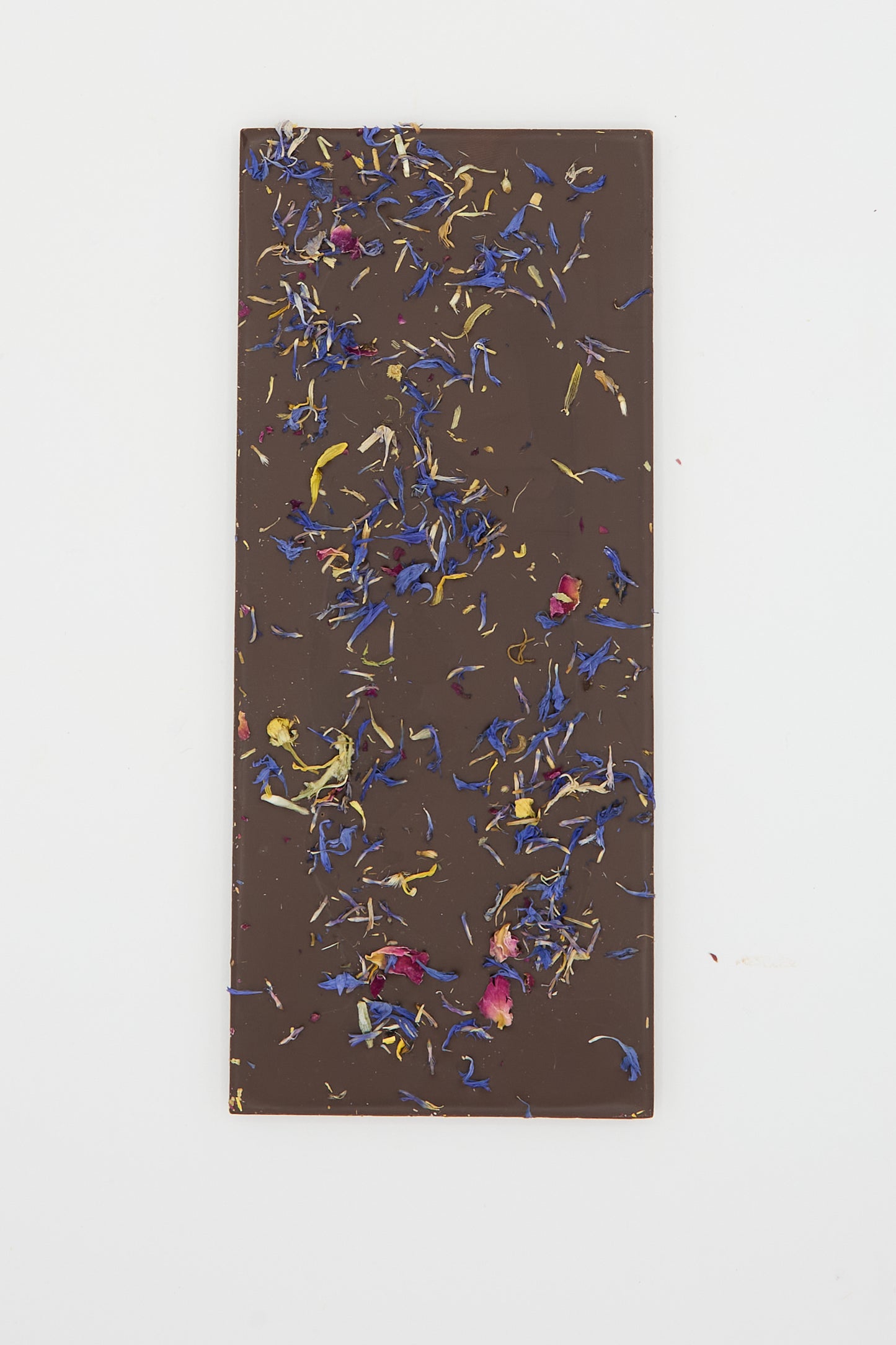 A rectangular piece of The Quiet Botanist's Wildflower Dream Bar, an Organic Dark Chocolate adorned with various colorful dried flower petals, set against a plain white background.