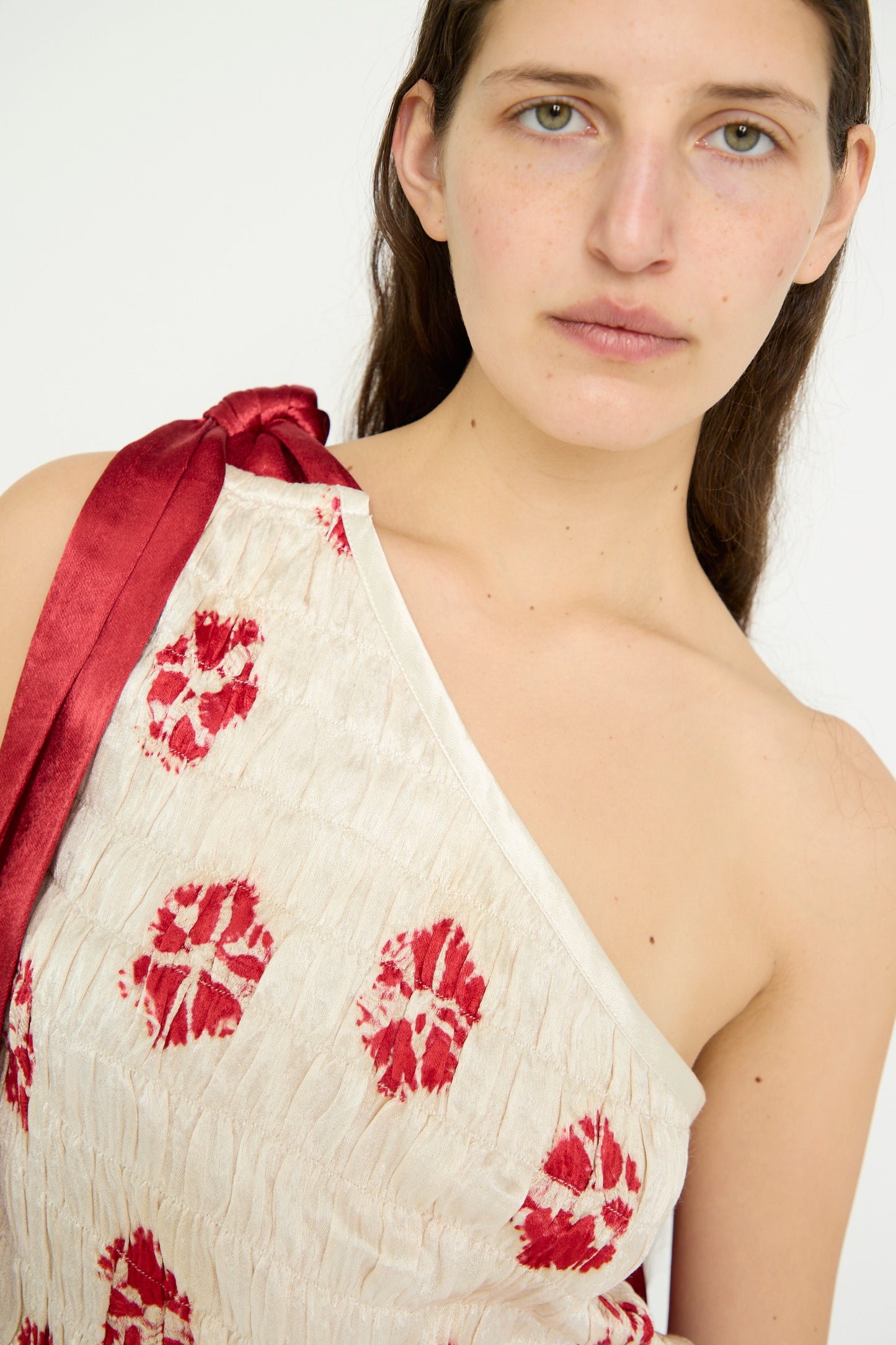 Someone wearing the TIGRA TIGRA Gathered Mashroo Knot Tie Top in white with red bandhej floral patterns and crinkled finish, staring into the camera.