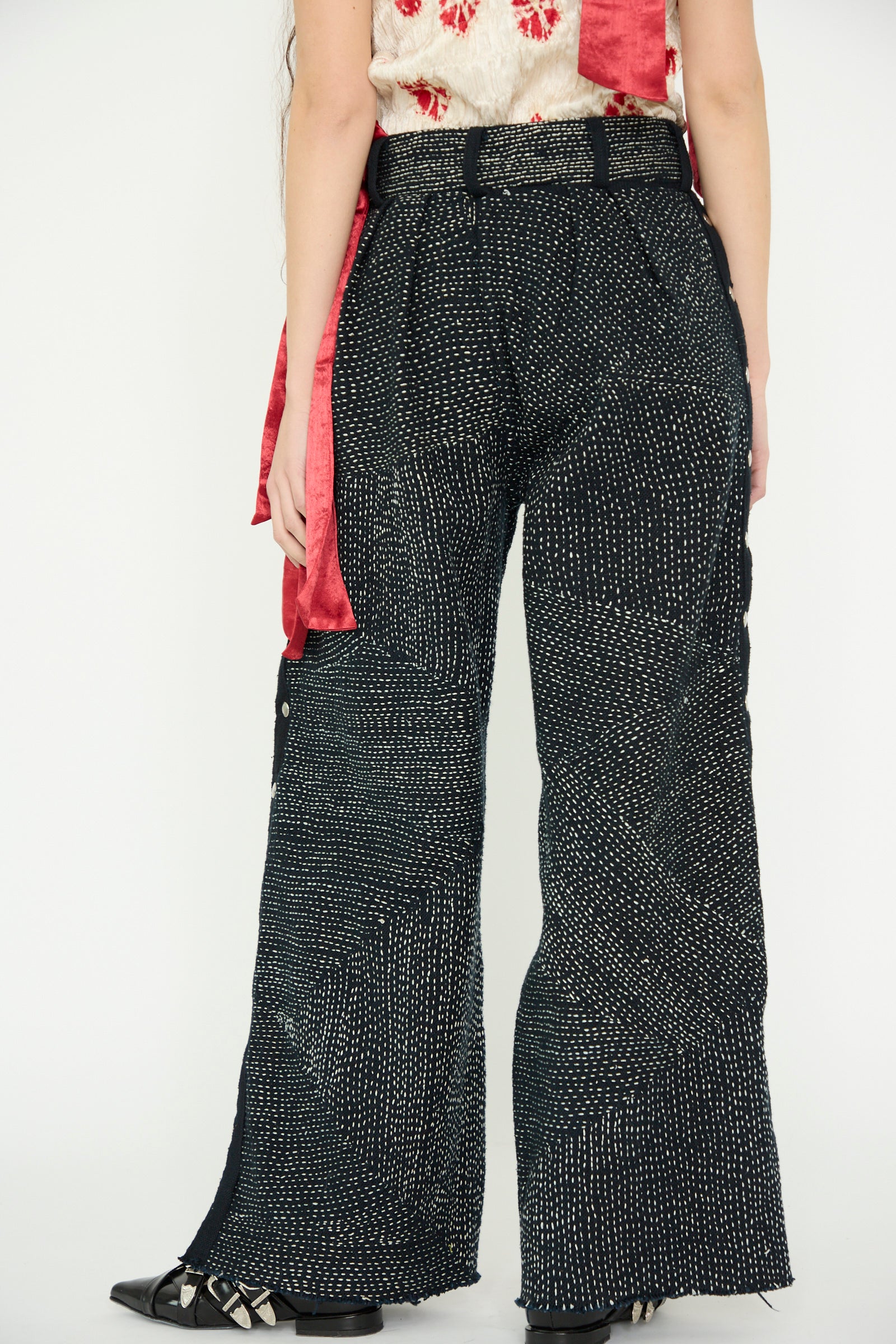 Against a light backdrop, a model wears the TIGRA TIGRA Heavy Khadi Kantha Snap Pant in Black with Cream. These wide-legged pants feature a dotted pattern and handwoven texture. 