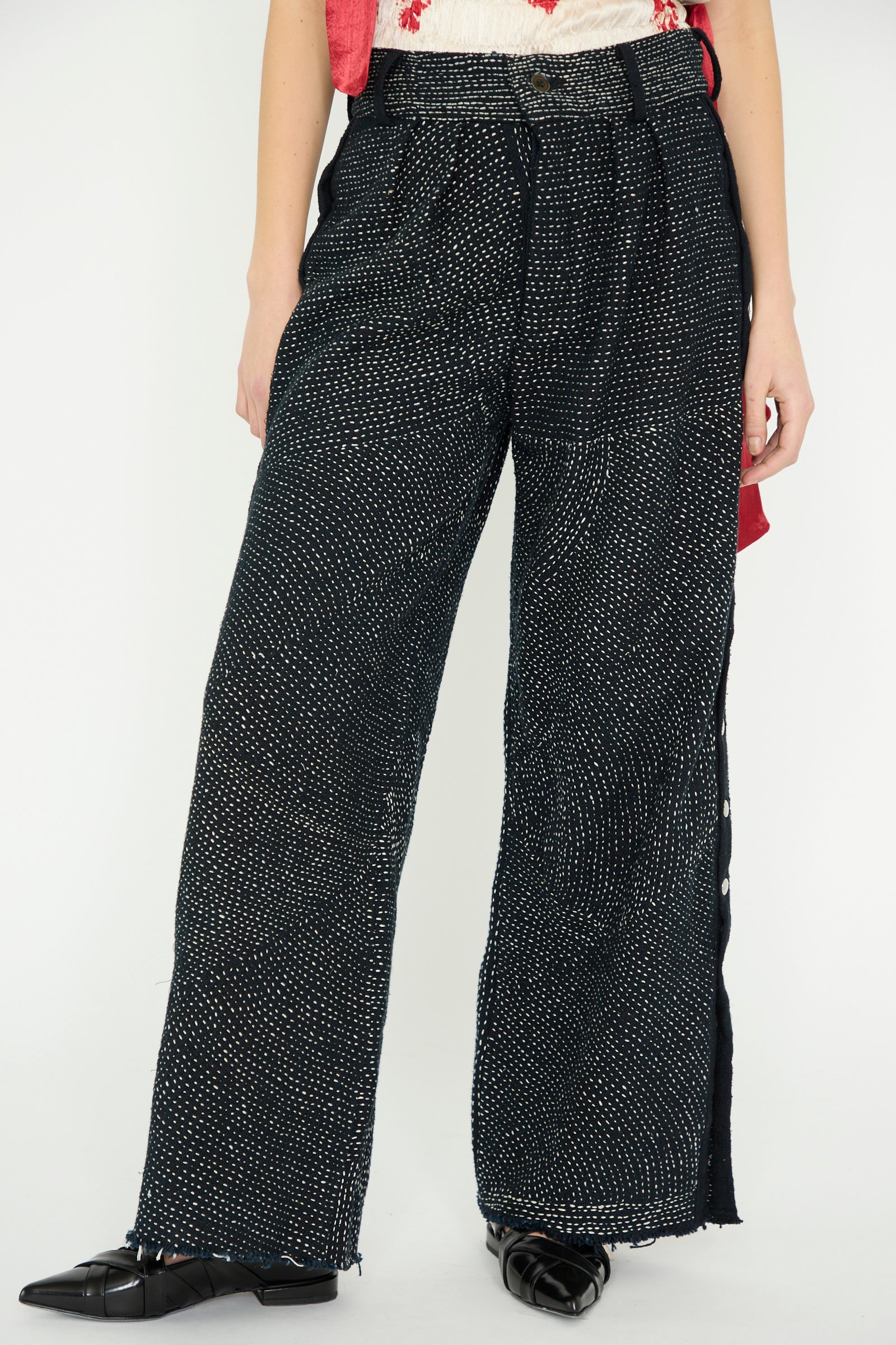 The TIGRA TIGRA Heavy Khadi Kantha Snap Pant in Black with Cream, paired with a white top featuring red accents and black shoes, worn by a model facing forward against a white background. 