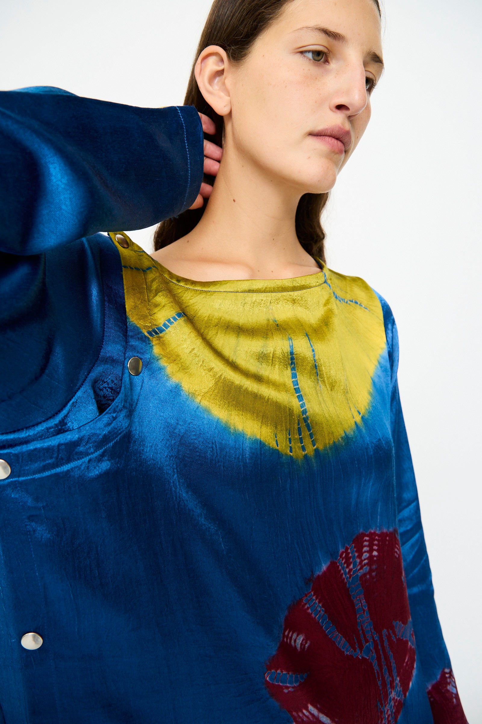 A woman in the TIGRA TIGRA Shibori Snap Dress in Jewel Blue, Acid Green, and Magenta looks off to the side with her hand behind her neck.