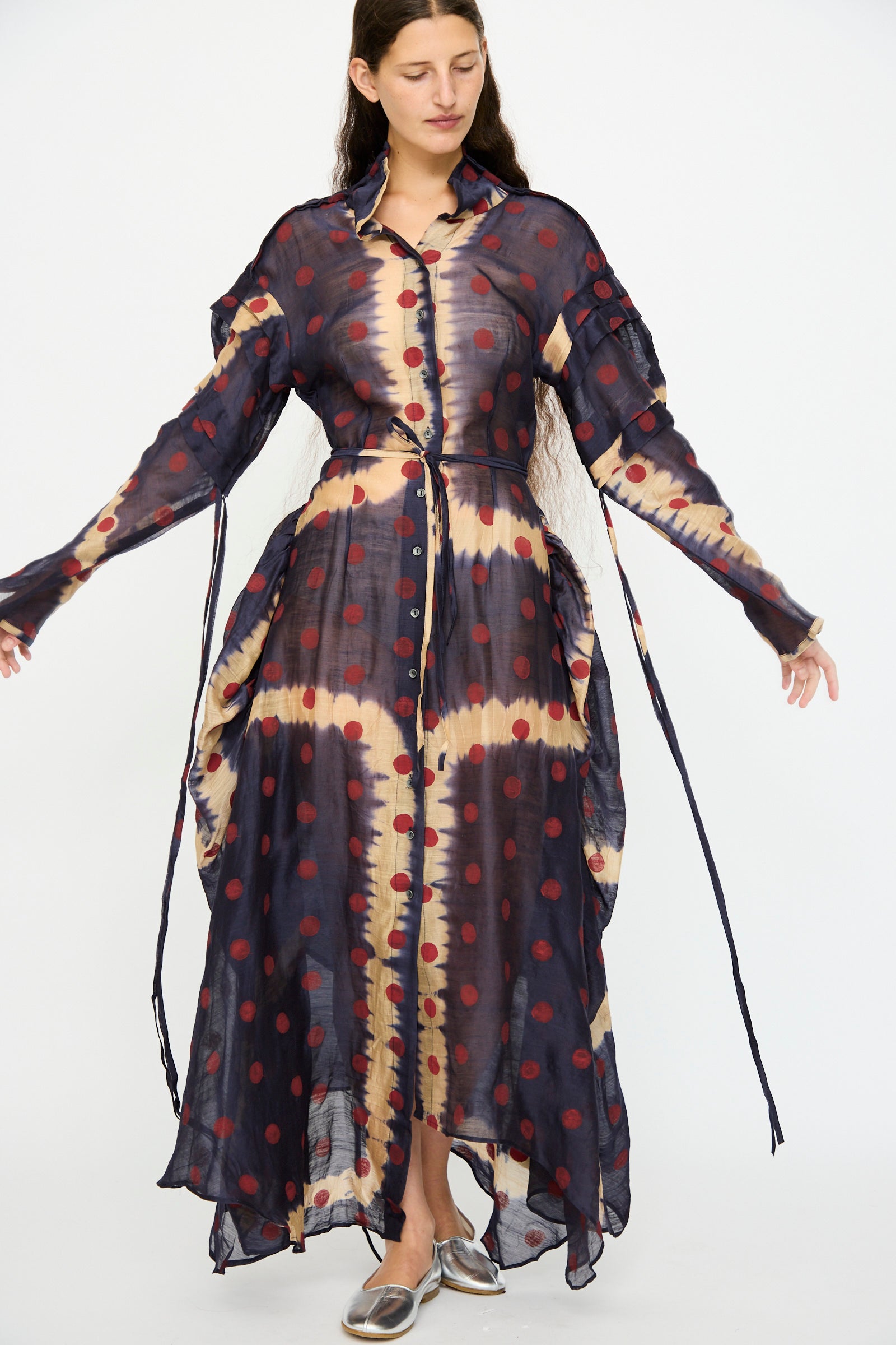 A woman wears the TIGRA TIGRA Silk Chanderi Teatime Dress in navy, cream, and red, featuring loose ties on the sleeves and sides, paired with metallic shoes.