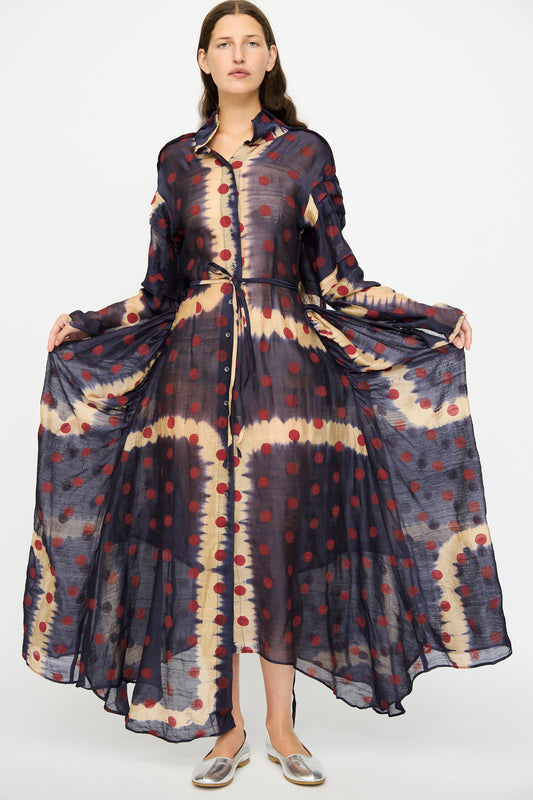 A woman wears the TIGRA TIGRA Silk Chanderi Teatime Dress in navy, cream, and red. She spreads out the flowing skirt, her straight brown hair down, and pairs the look with silver flats.