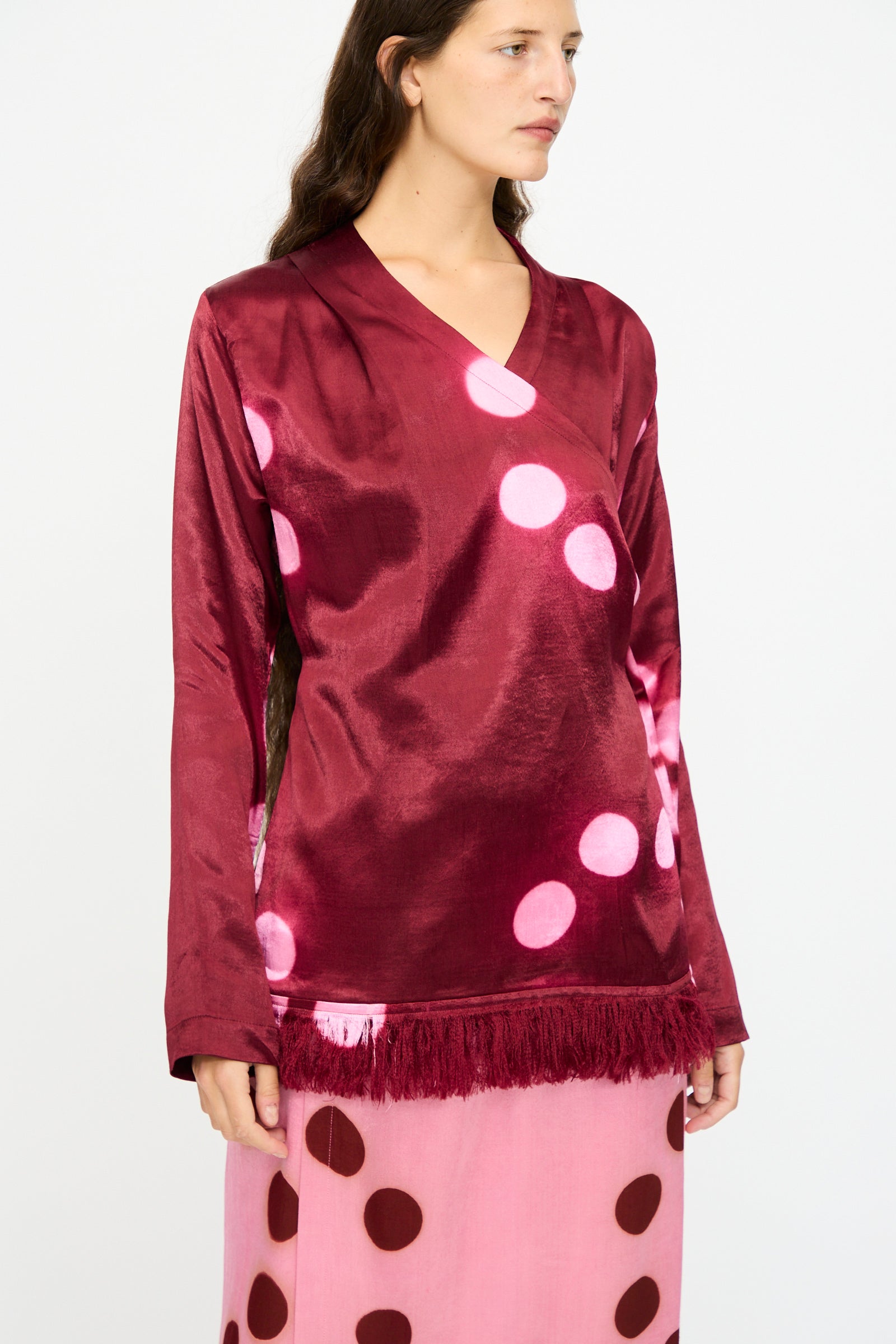 A person wearing the TIGRA TIGRA Silk Mashroo Moon Dye Wrap Top in Maroon, paired with a pink skirt featuring brown polka dots.