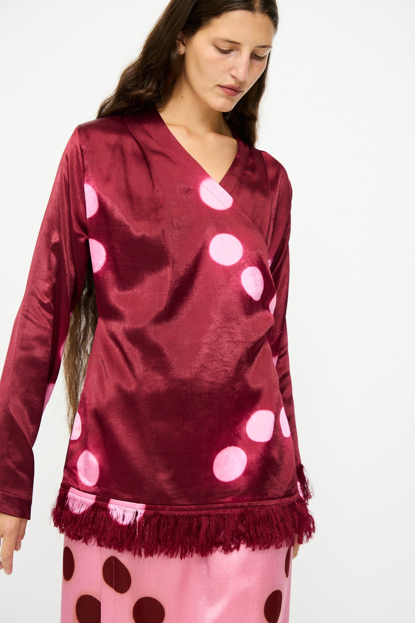 A woman wears the TIGRA TIGRA Silk Mashroo Moon Dye Wrap Top in Maroon, styled with a pink skirt featuring large red polka dots.
