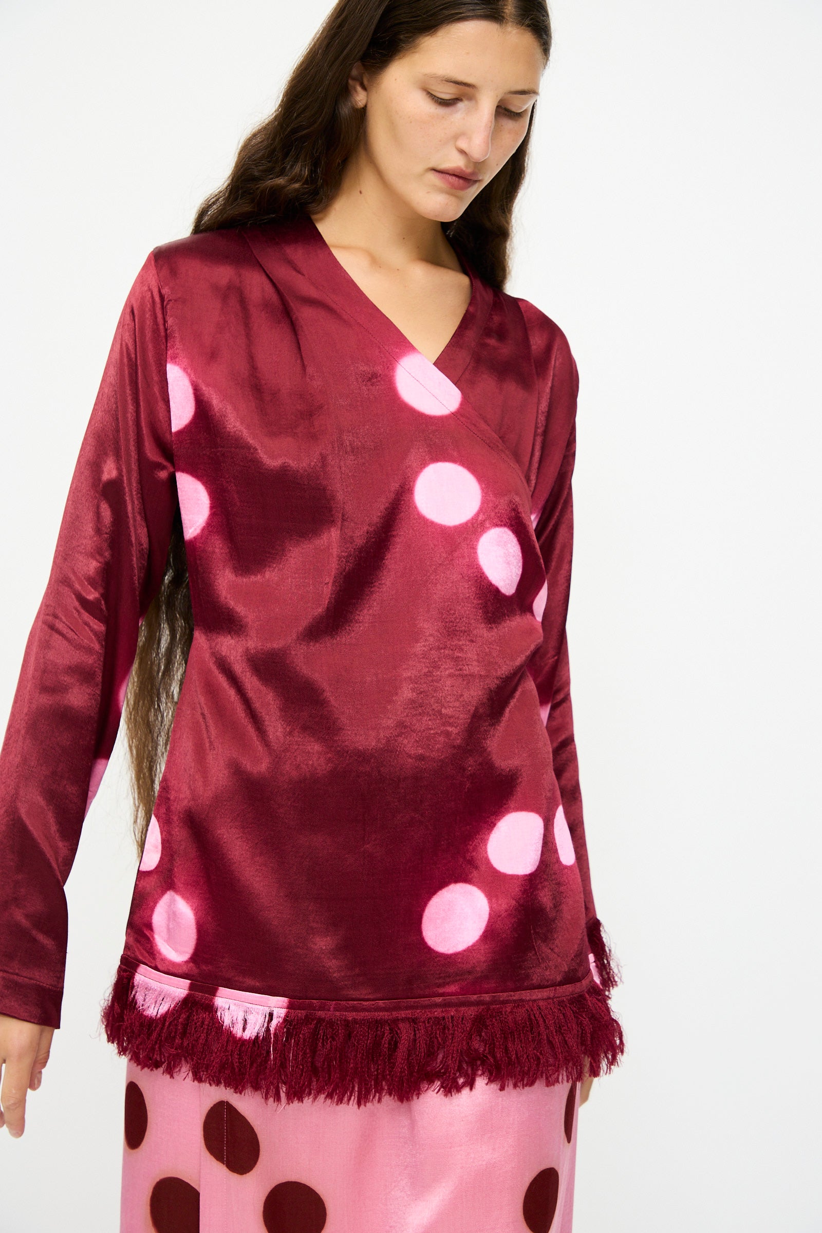 A woman wears the TIGRA TIGRA Silk Mashroo Moon Dye Wrap Top in Maroon, styled with a pink skirt featuring large red polka dots.