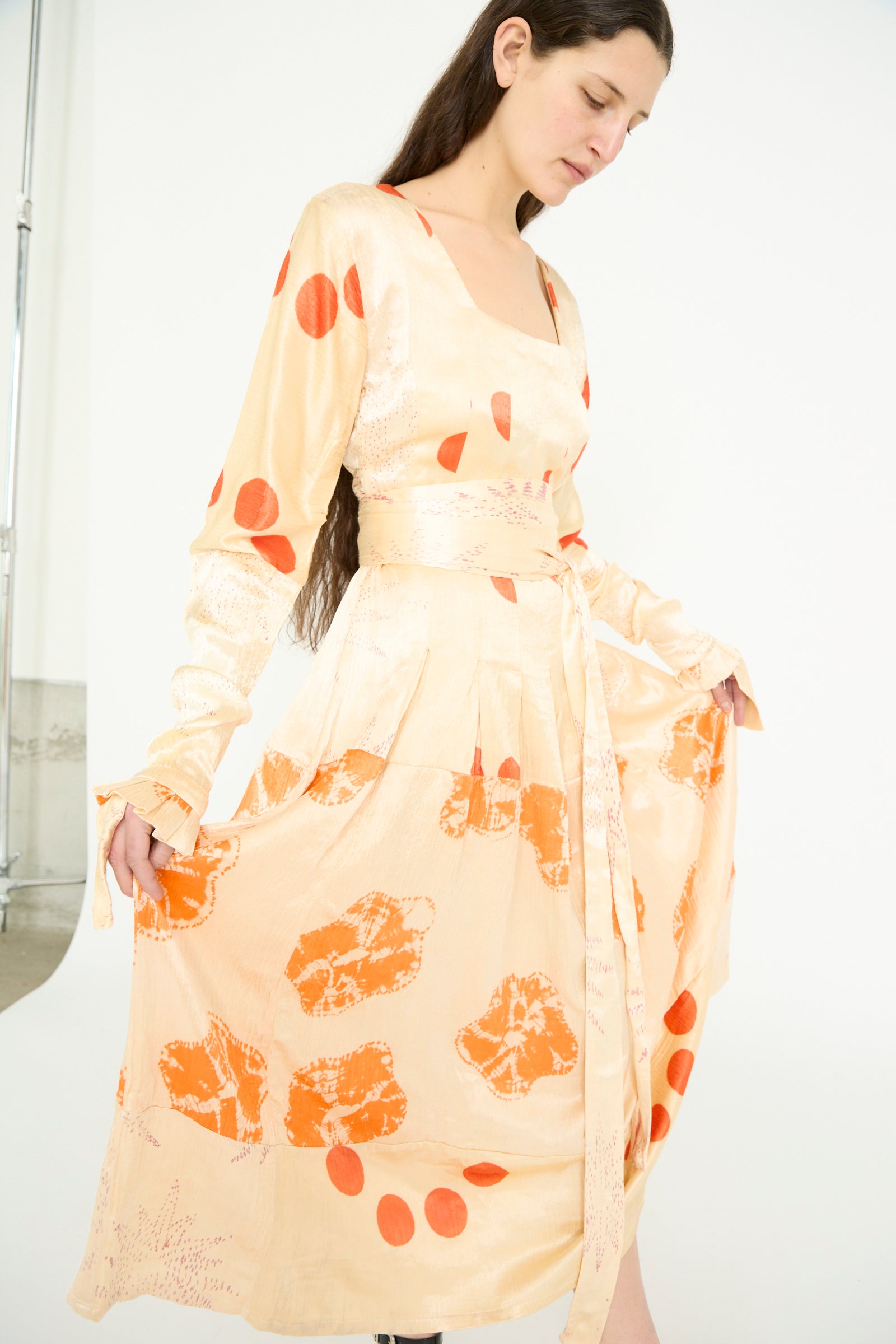 A model in a TIGRA TIGRA Tropical Dress featuring a long-sleeved design with tie-dyed patchwork in pale grey and orange bandhej stands against a white background.