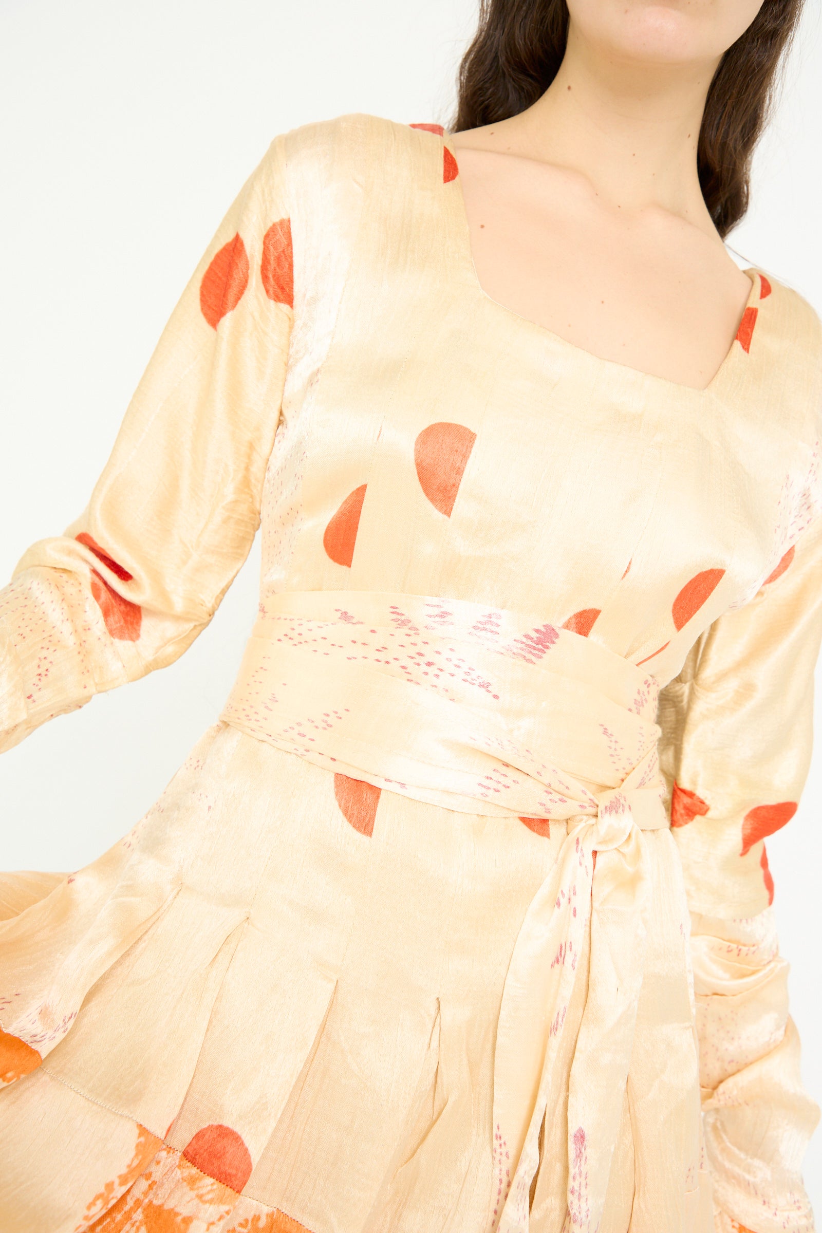 A model is seen close-up in TIGRA TIGRA's Tropical Dress, a pale yellow and orange Bandhej patchwork tie-dye featuring red polka dots and a square neckline against a white backdrop. 