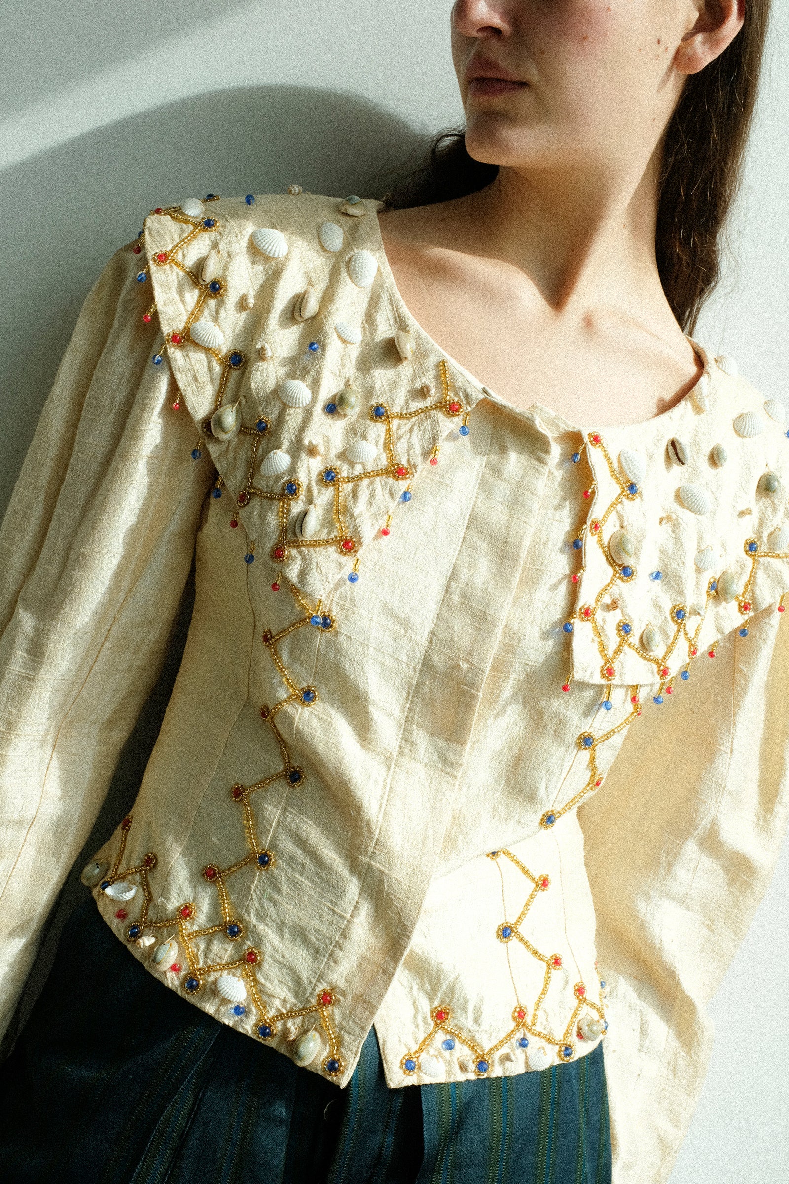 Woman wearing the tigra tigra cream-colored embroidered blouse with a white background.