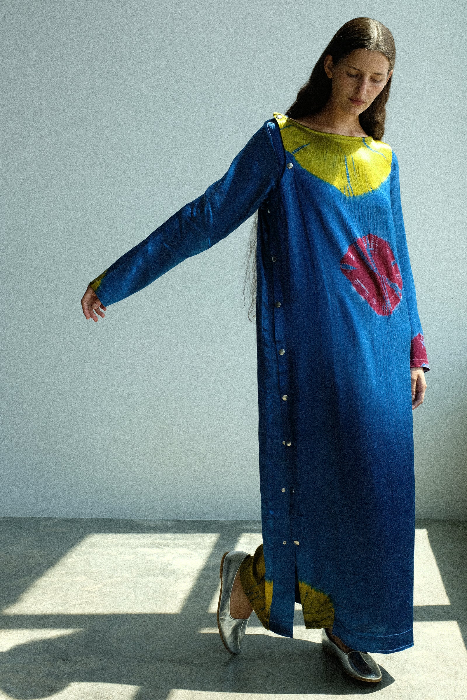 Woman wearing a long blue dress with colorful patterns in a minimalistic setting