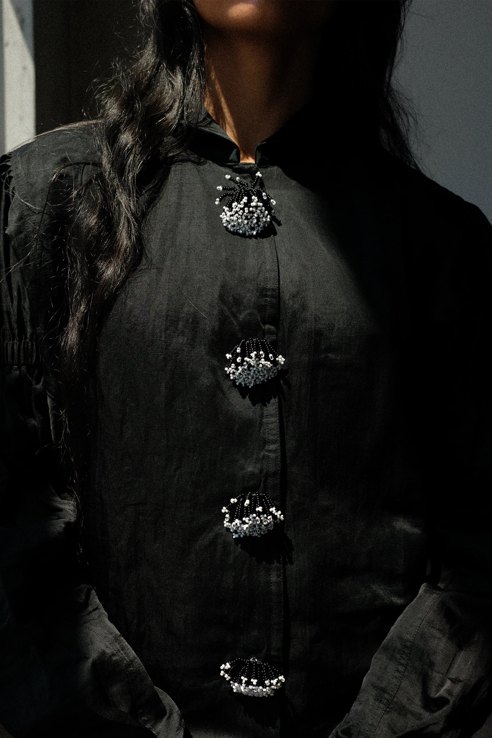 Close-up of a person wearing a black button-front top with ornate silver embellished buttons.