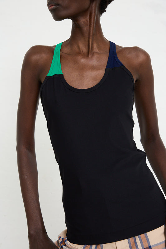 A person wearing the TOGA ARCHIVES High Stretch Tank Top in Black with green and blue shoulder straps, posing against a white background. The slim fit tank highlights their physique, crafted in stretch nylon for comfort and style.