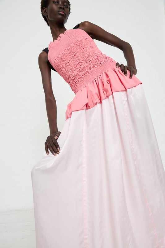 A person in a Shirring Satin Dress in Pink by TOGA ARCHIVES, featuring a sleeveless design with a square neck and ruffled top, poses gracefully against a plain white background.