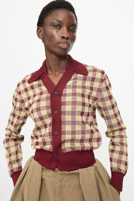 A model wears the TOGA ARCHIVES Check Knit Cardigan in Dark Red, buttoned up, paired with beige high-waisted trousers, standing against a plain white background.