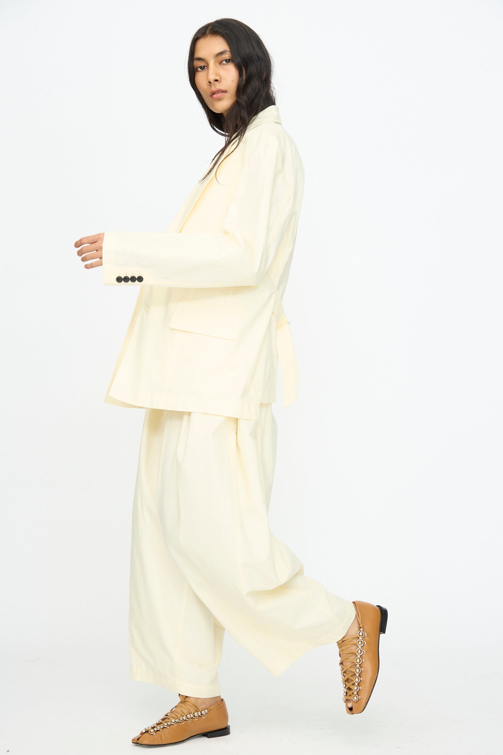 Wearing the Cotton Ox Jacket in Off White by TOGA ARCHIVES and wide-leg pants with tan shoes, this look stands out against a plain white background; the relaxed jacket brings effortless style.