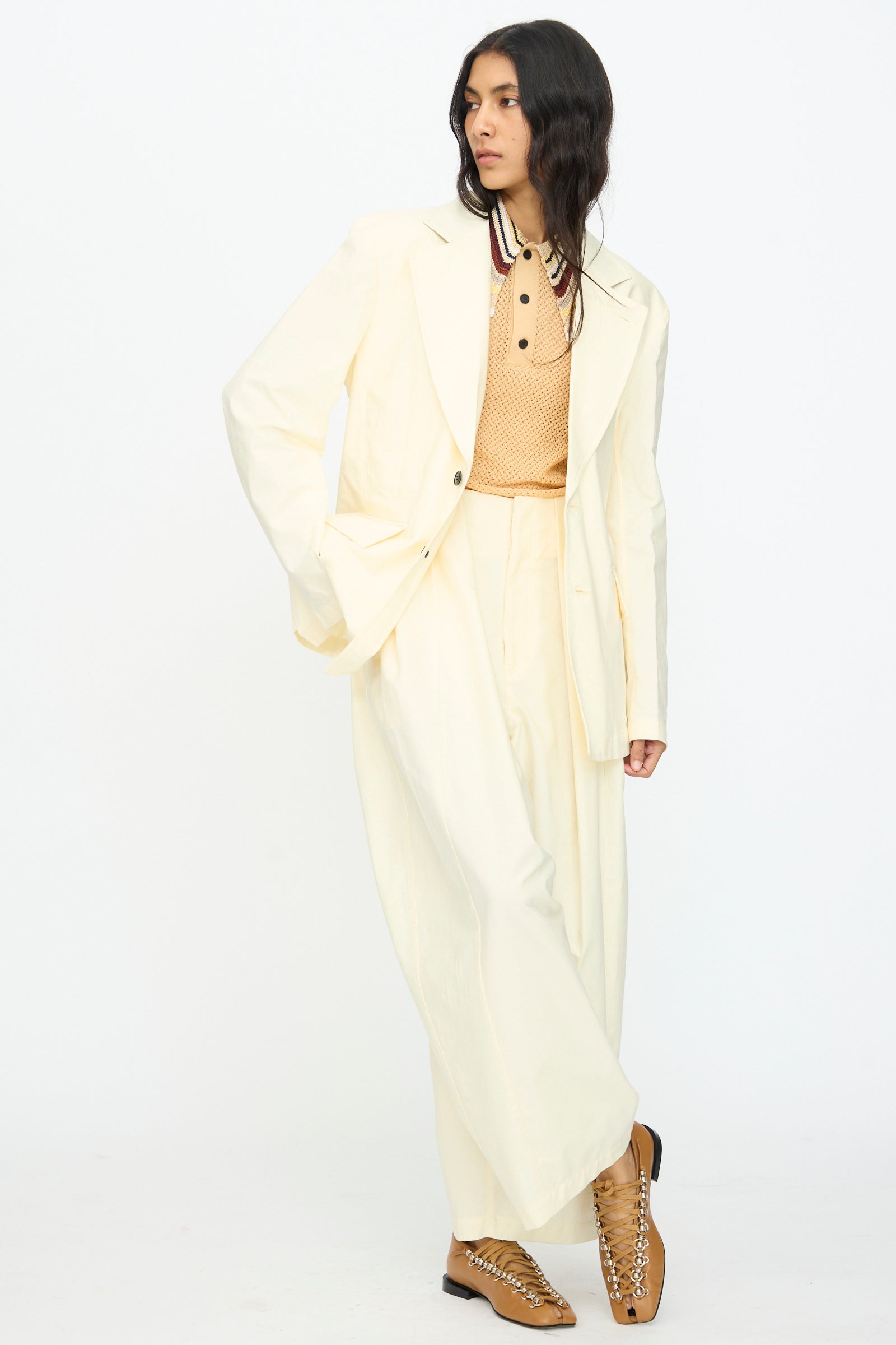 A person wears the TOGA ARCHIVES Cotton Ox Jacket in Off White, paired with wide-leg pants, a beige polo shirt, and tan lace-up shoes, standing against a plain white background. Made in Japan.